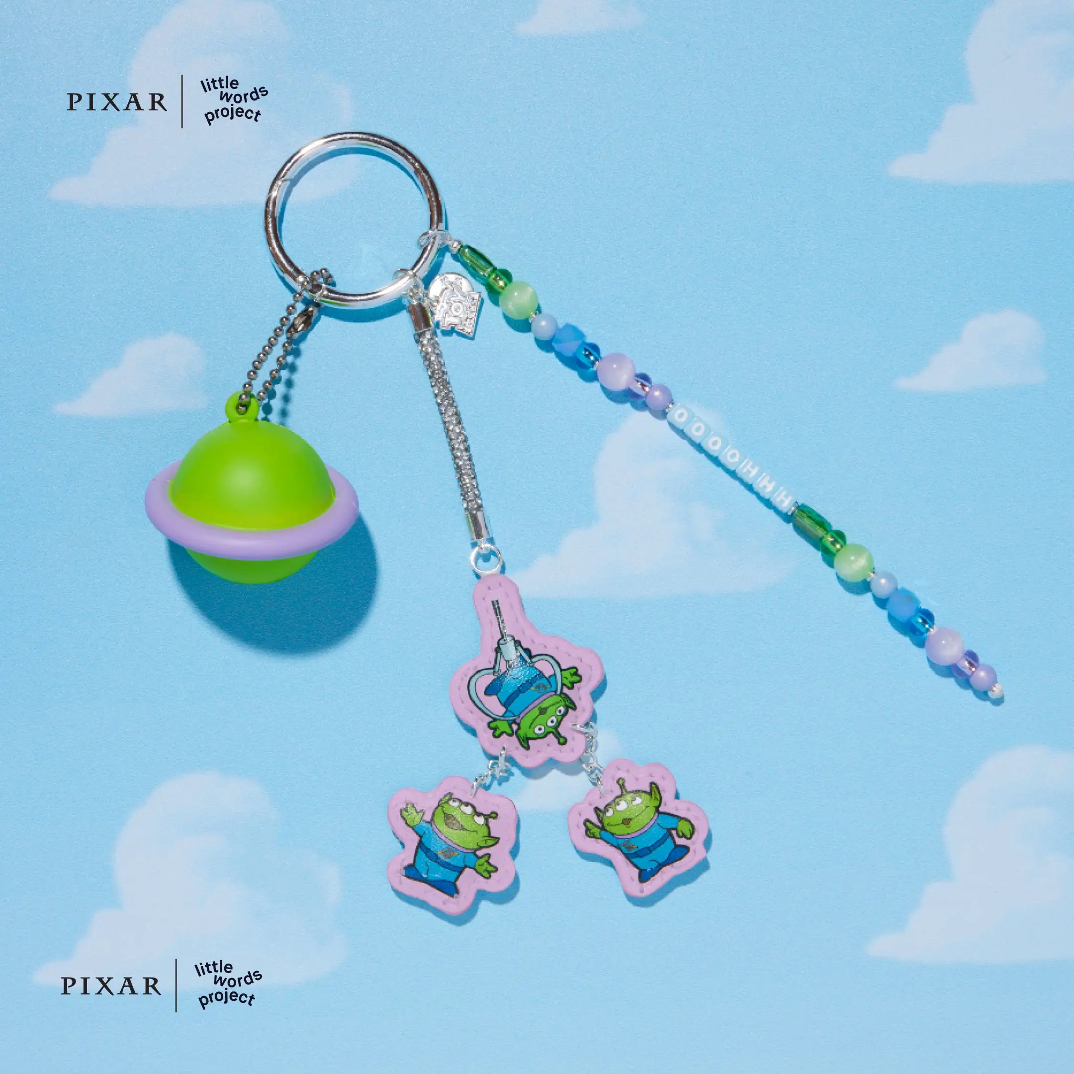Keychain with alien charms and a green planet charm on a blue background with cloud patterns, featuring Pixar branding.