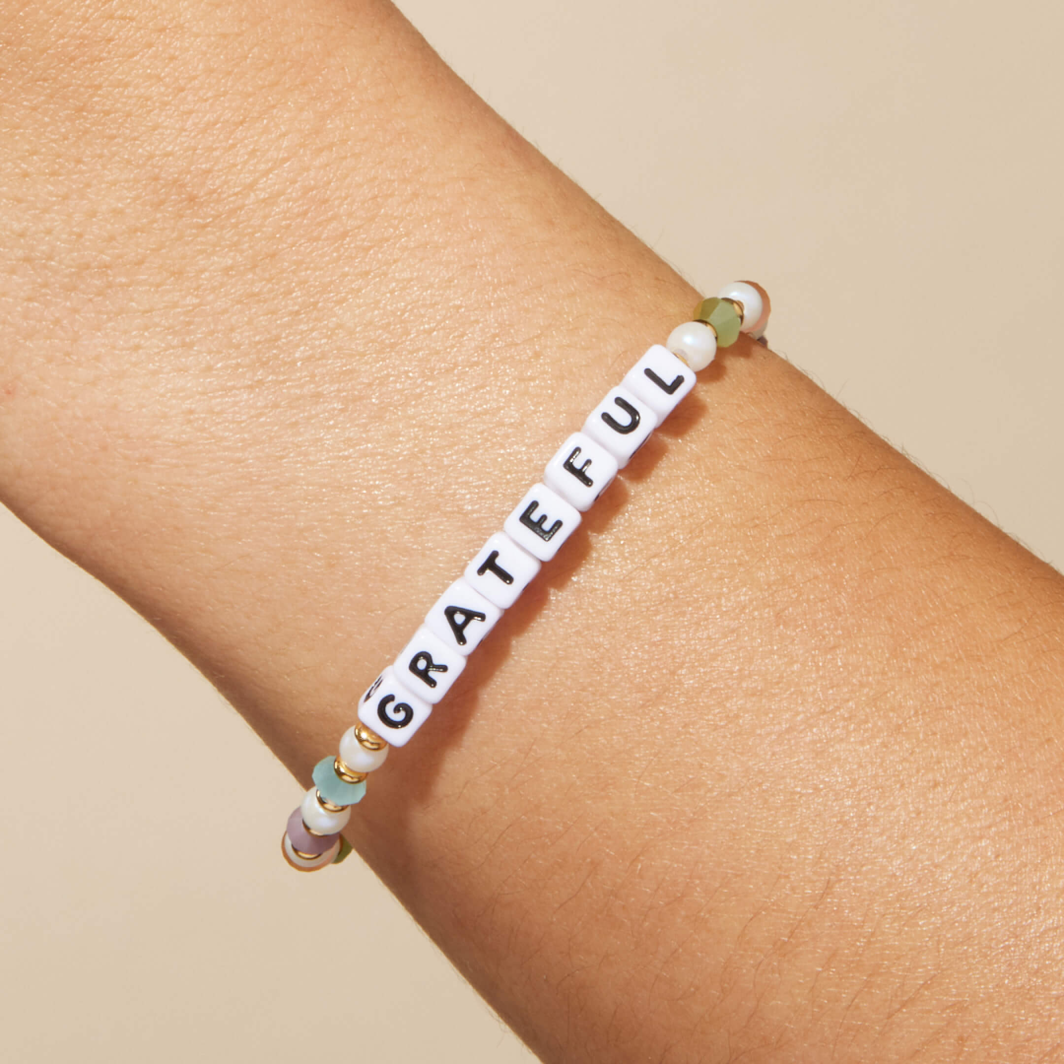 Bracelet with 'GRATEFUL' beads on a wrist against a beige background