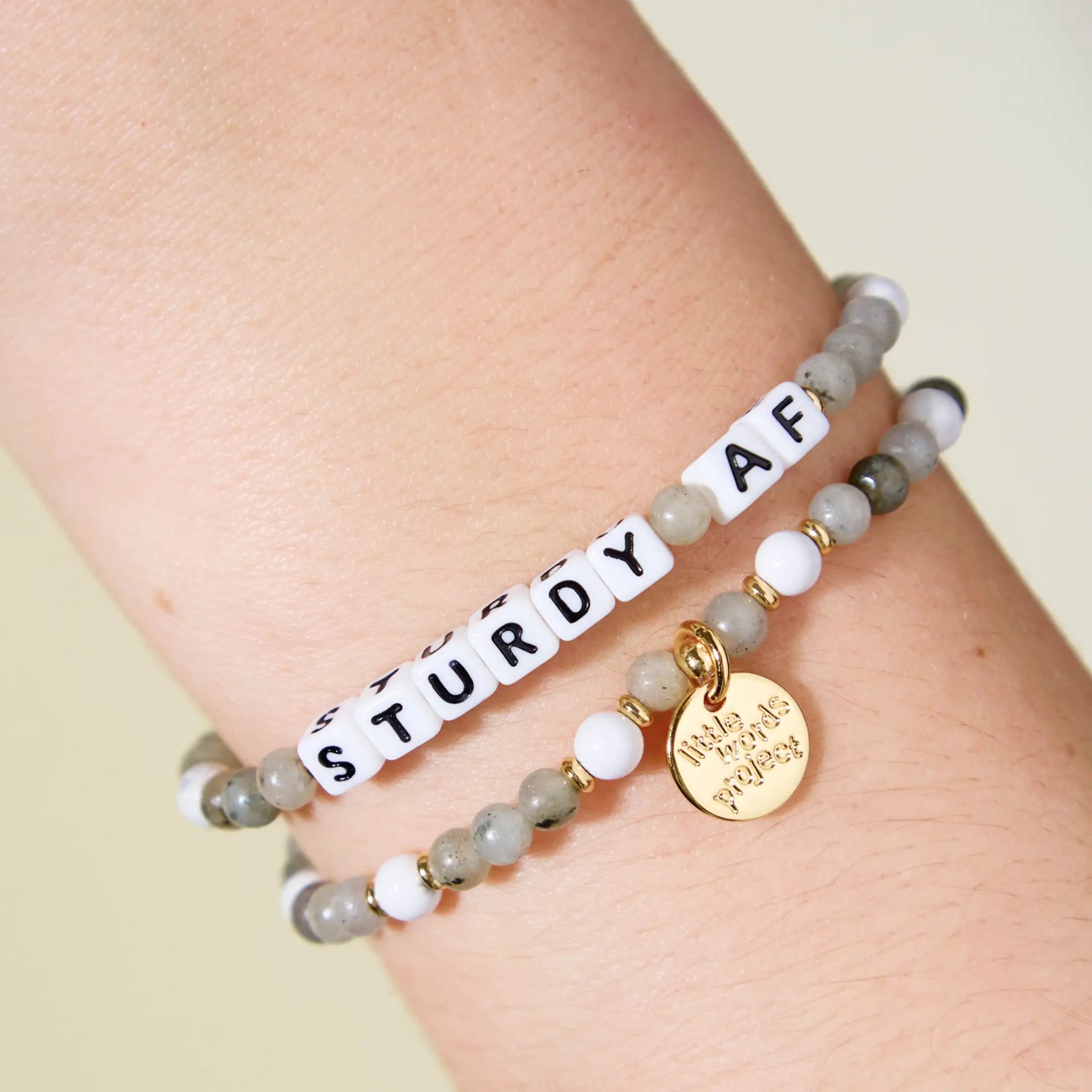 Bracelets with 'STURDY AF' and gold tag on a wrist against a light background