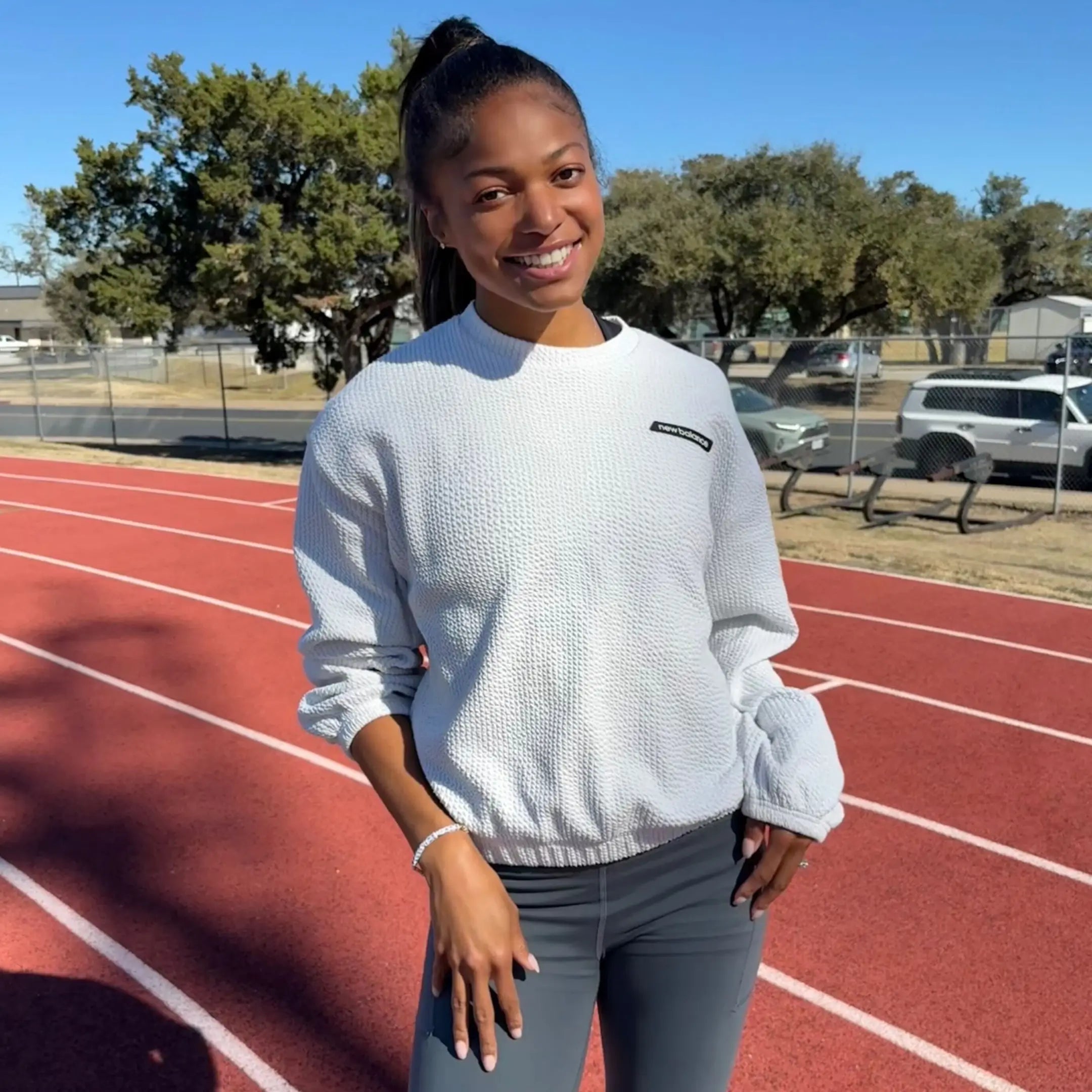 Person wearing a light gray sweatshirt and dark gray leggings on a track field.