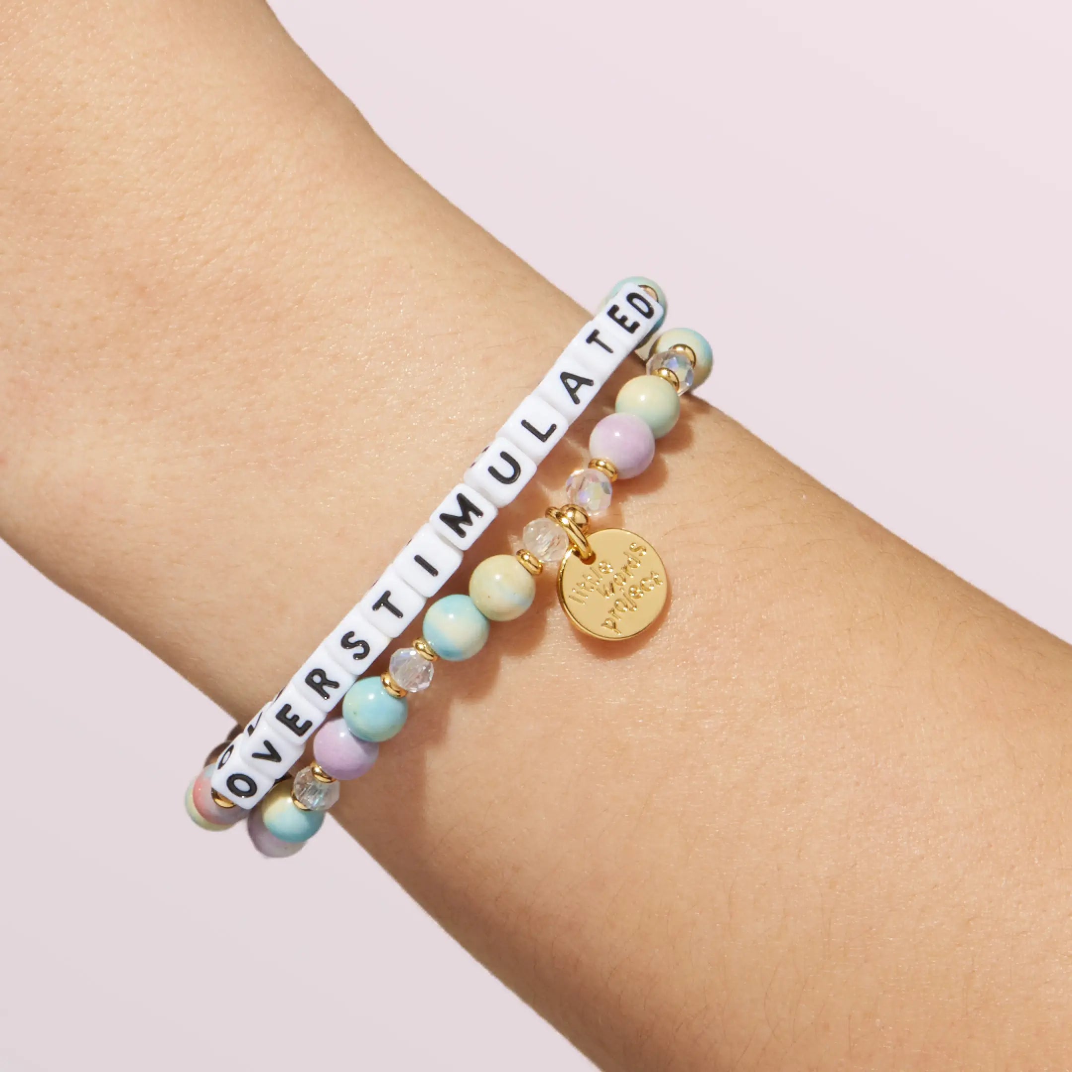 Bracelet with pastel beads and a gold tag on a wrist against a light background