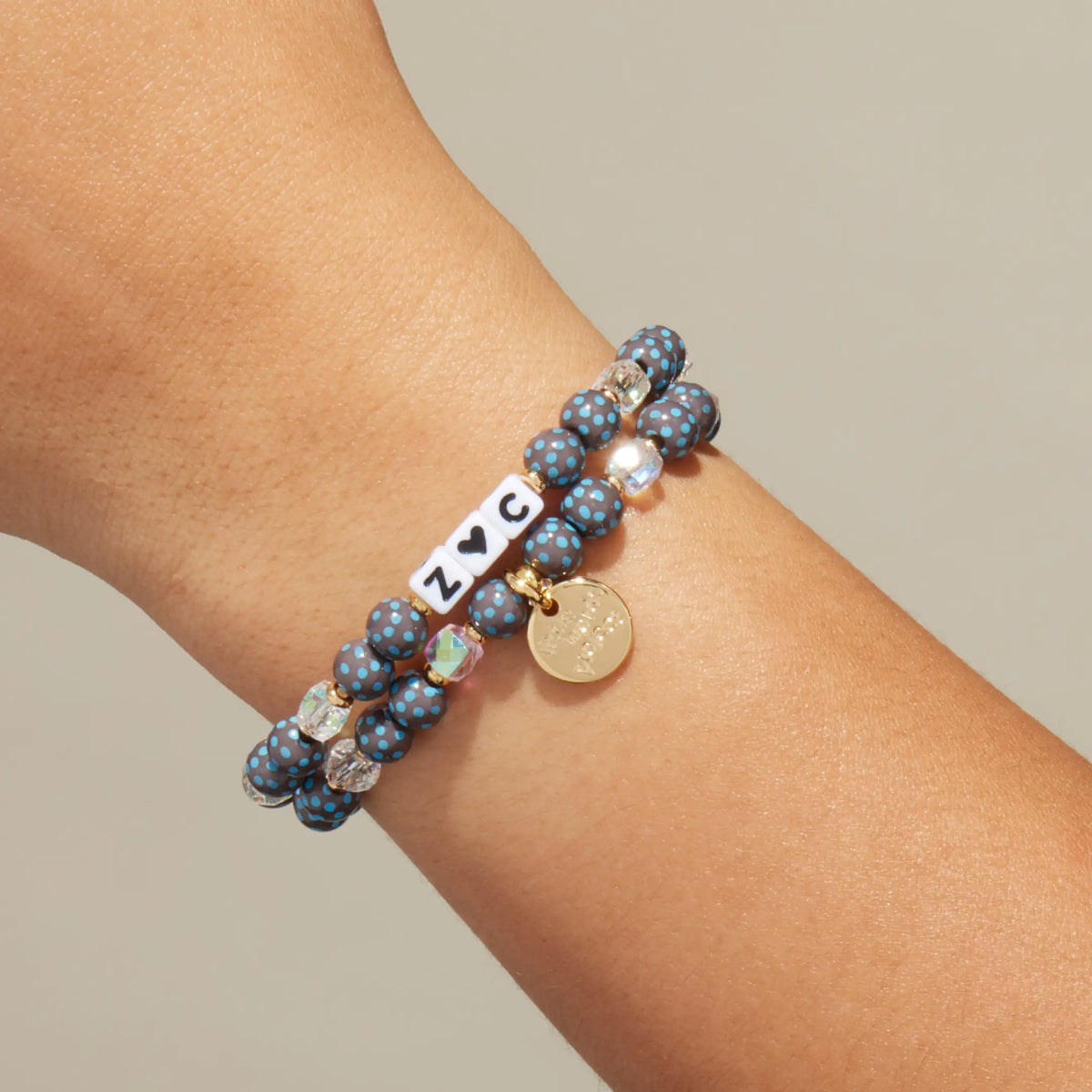 Custom Polky Babe bracelet worn on a wrist, white letter beads spelling Z heart C with dark gray beads with blue polka dots