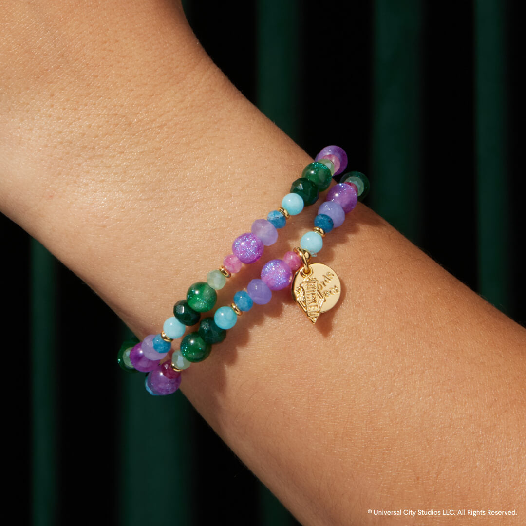 Multicolored beaded bracelet with a gold charm on a wrist against a dark background