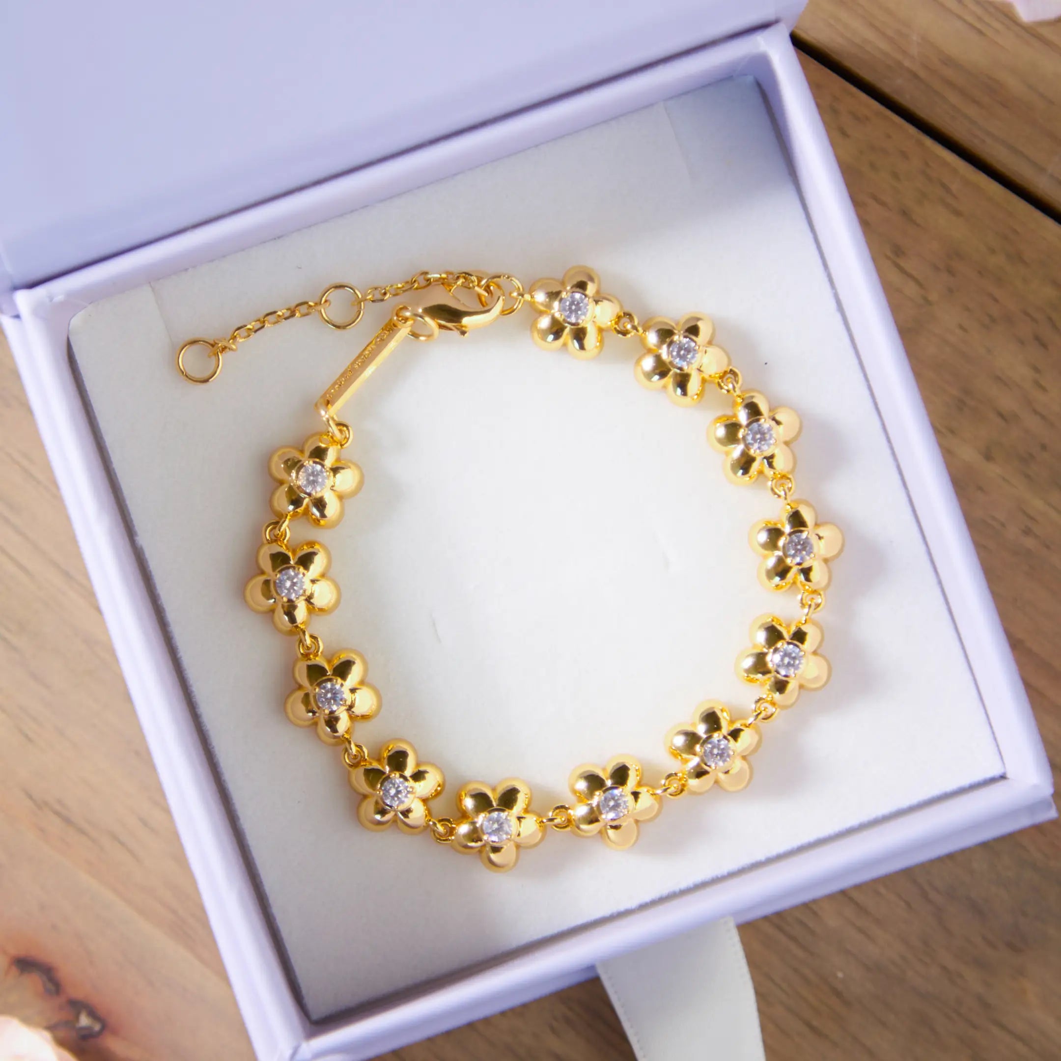 Gold bracelet with floral design in a white box on a wooden surface