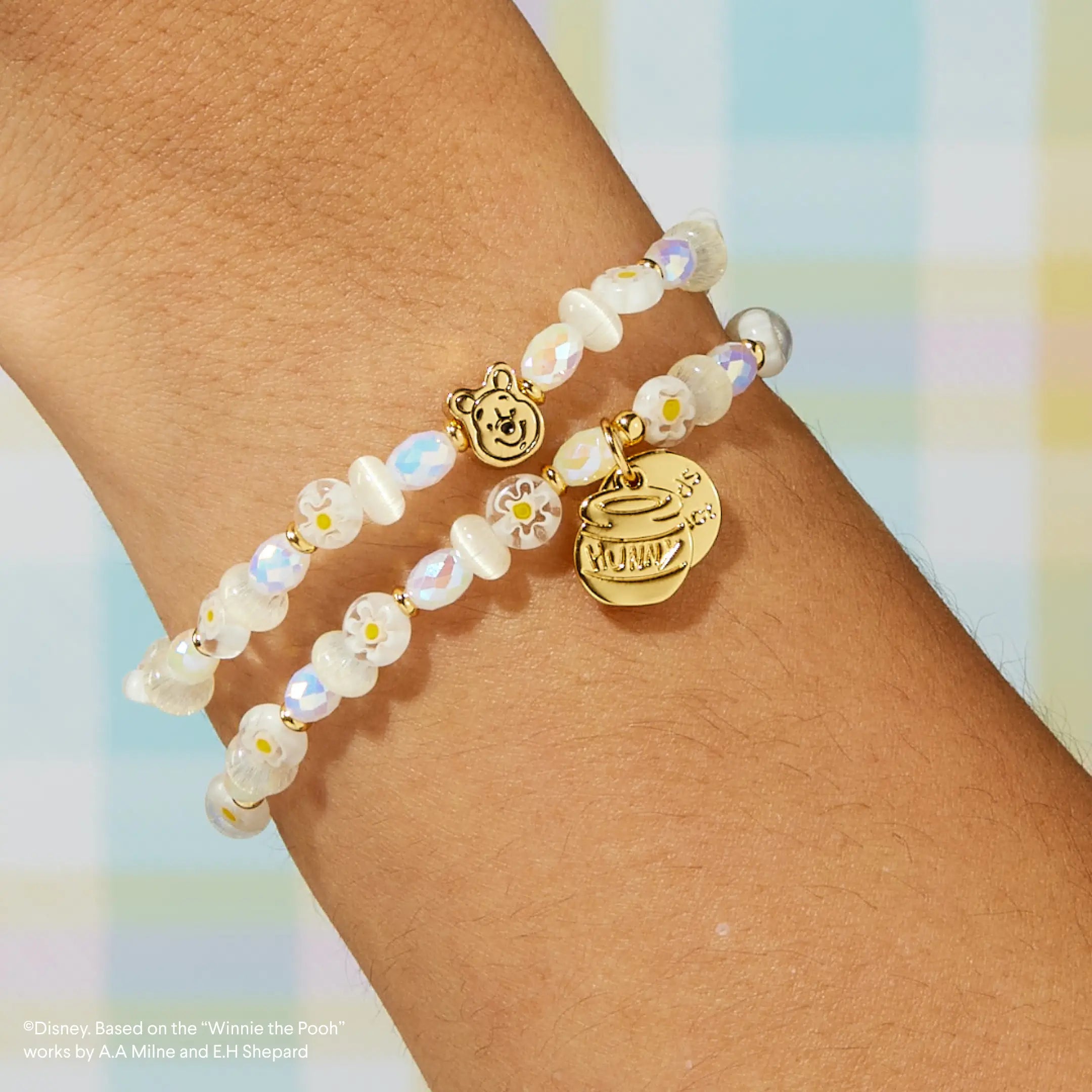 Bracelet with a gold tag on a wrist against a pastel background