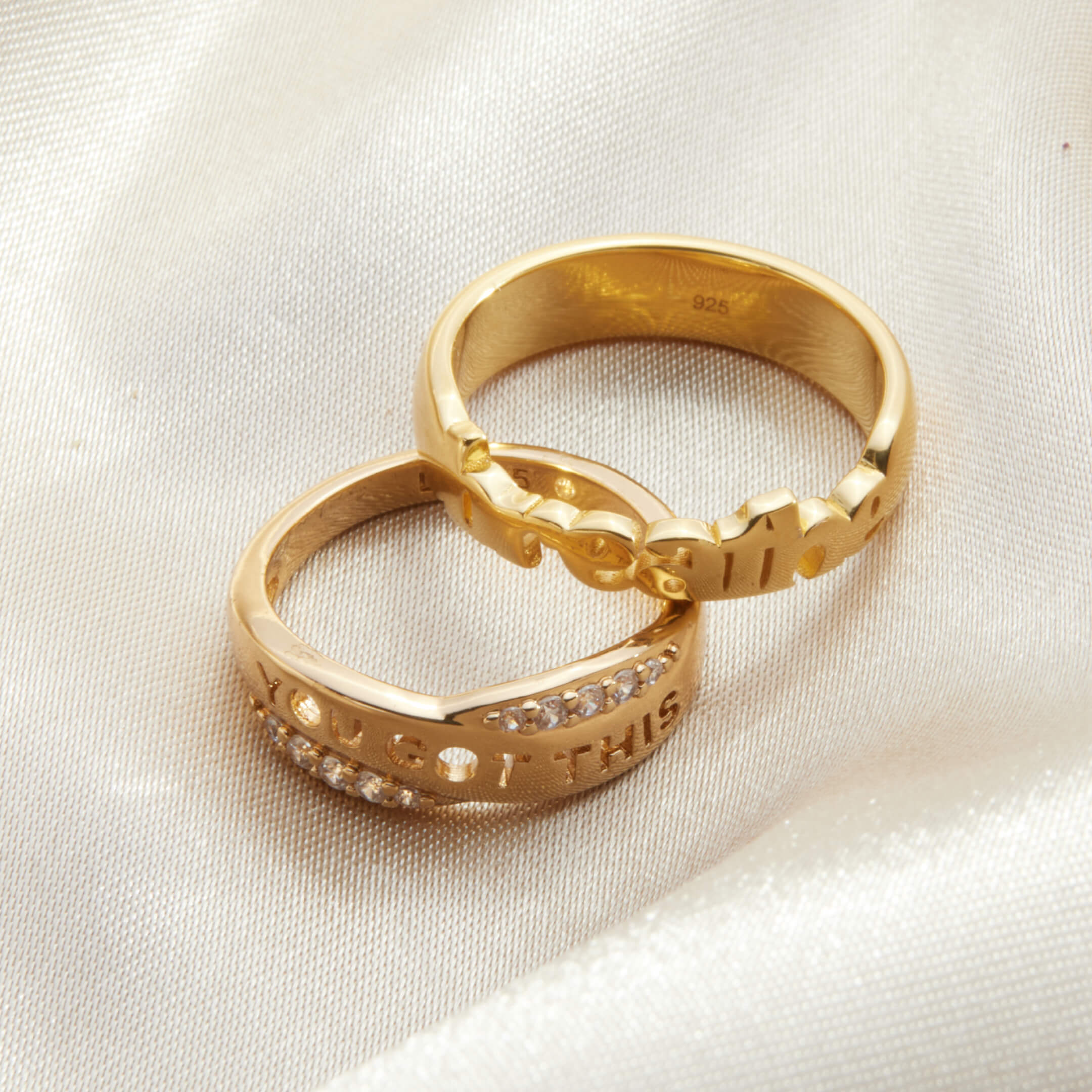 Two gold rings with engraved text on a light fabric background