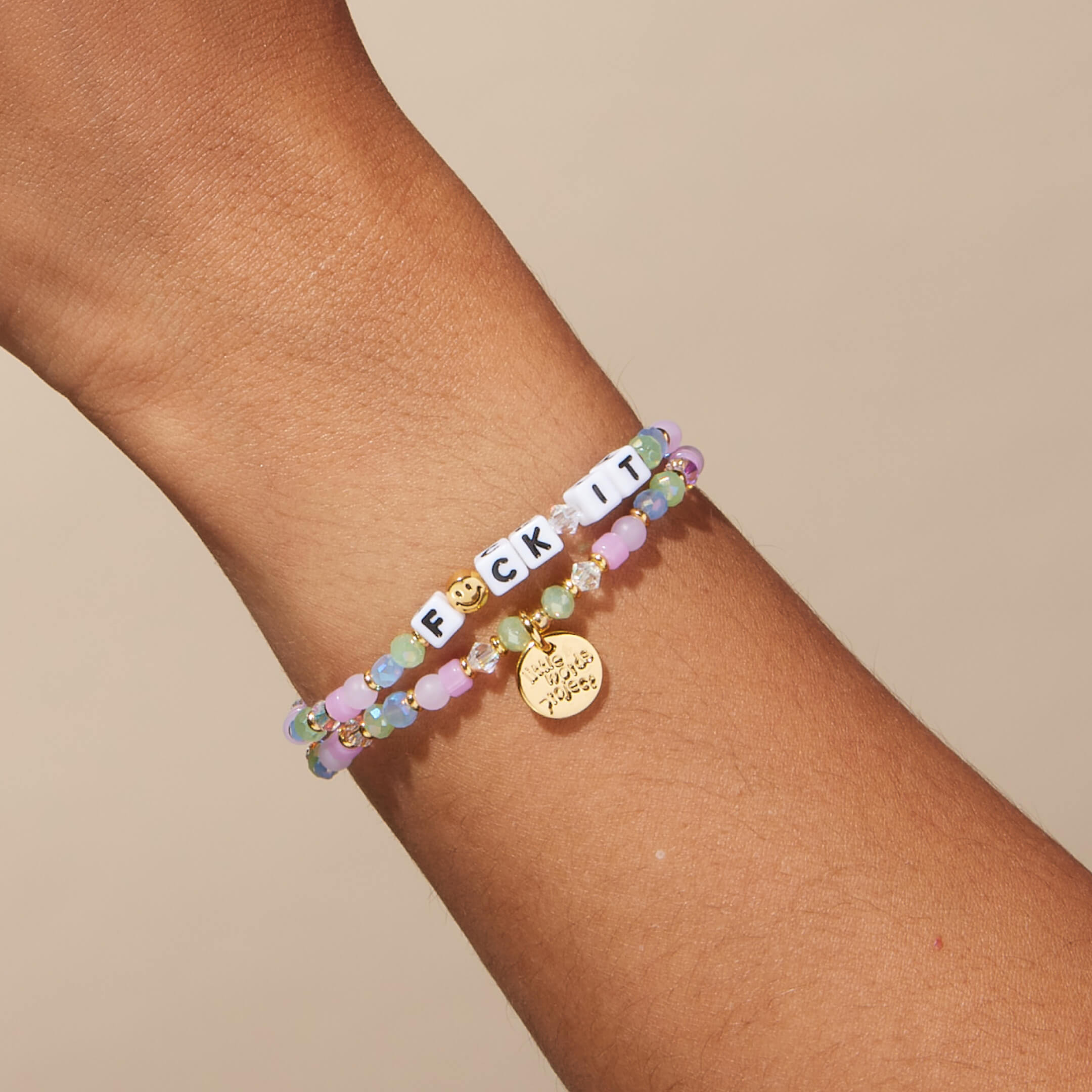 Multicolored beaded bracelet with a gold charm on a wrist against a beige background