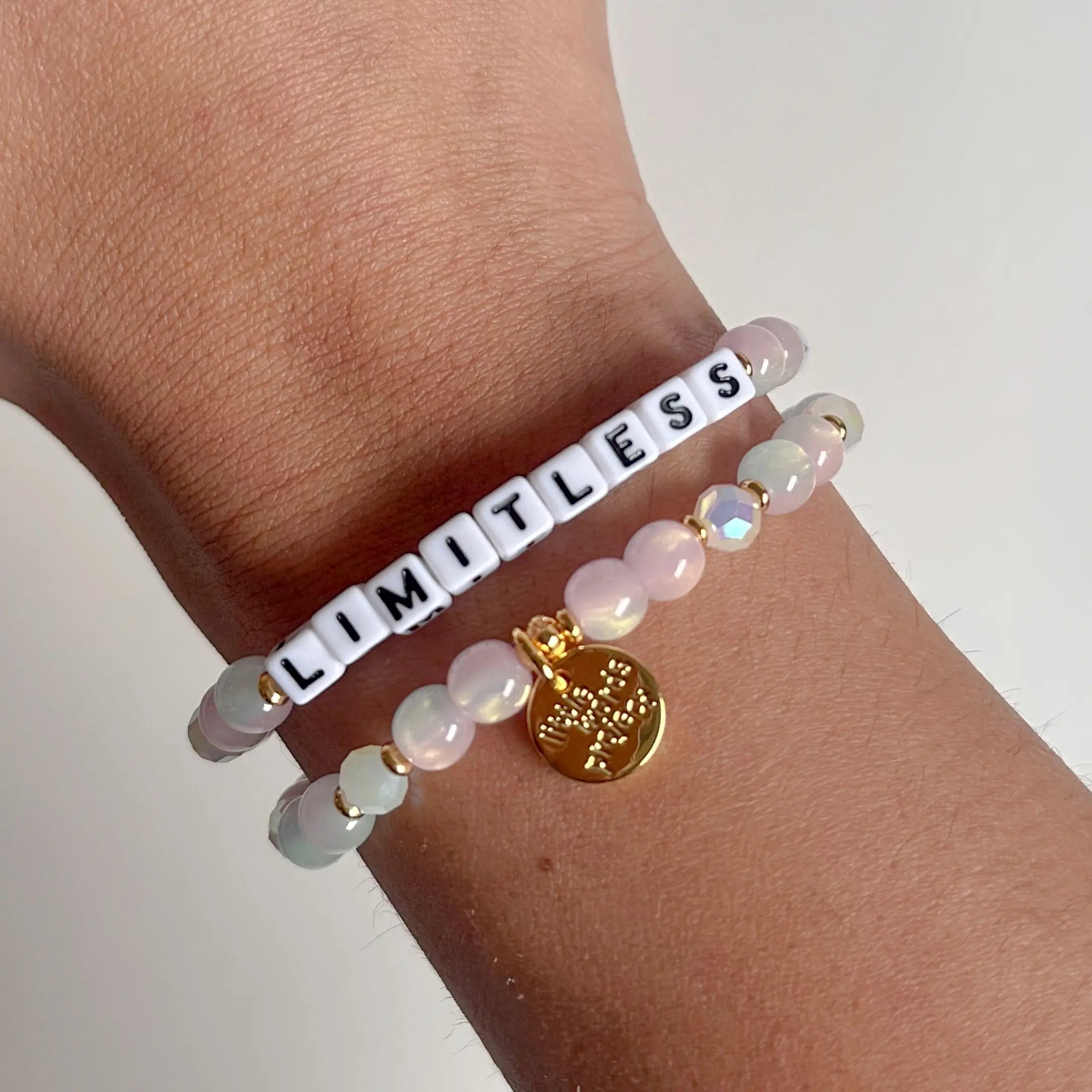 Bracelet with 'LIMITLESS' and a gold tag on a wrist against a white background
