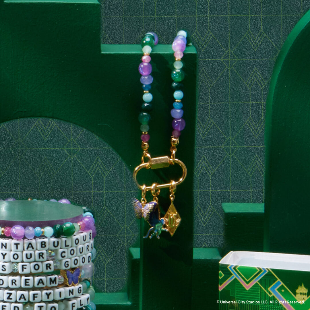 Colorful beaded bracelet with charms on a green stand against a green geometric-patterned background.