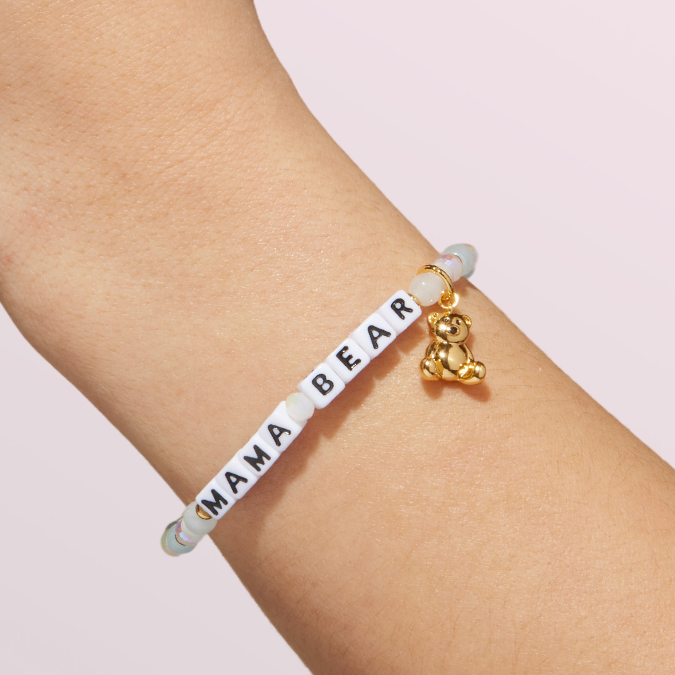 Bracelet with 'MAMA BEAR' and a bear charm on a wrist against a light background