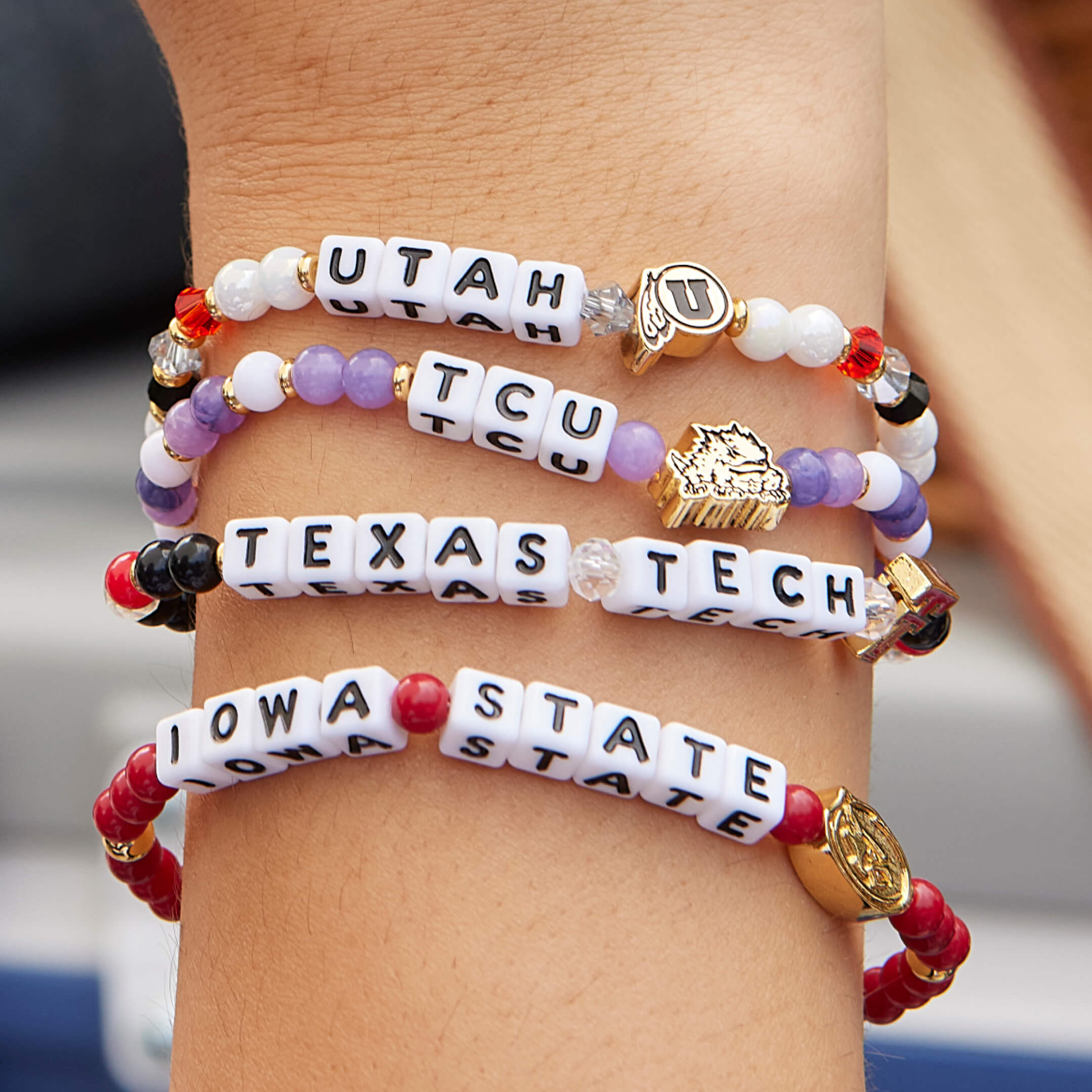 Bracelets with letter beads on a wrist, featuring universities.