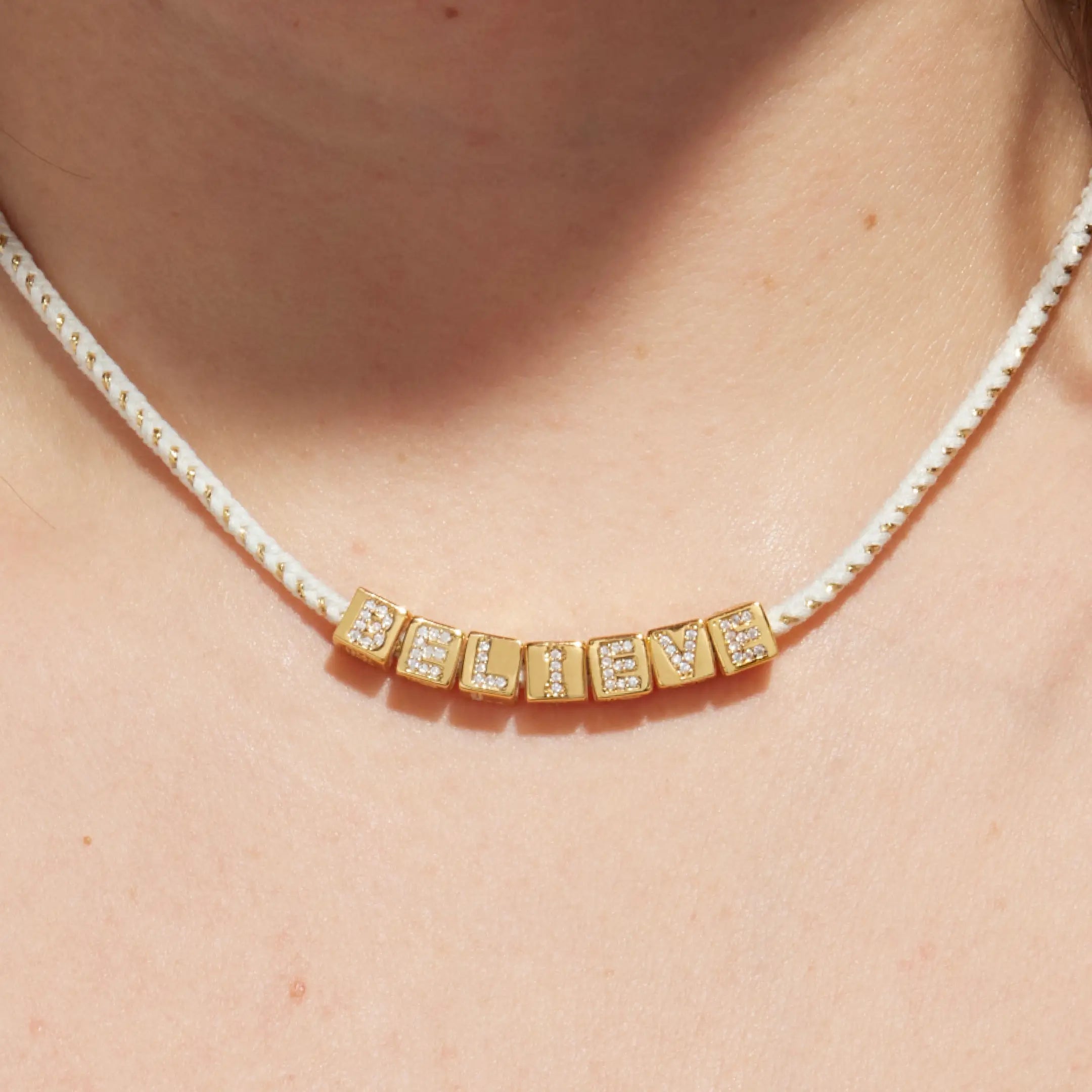 Necklace with gold 'BELIEVE' on a person's neck