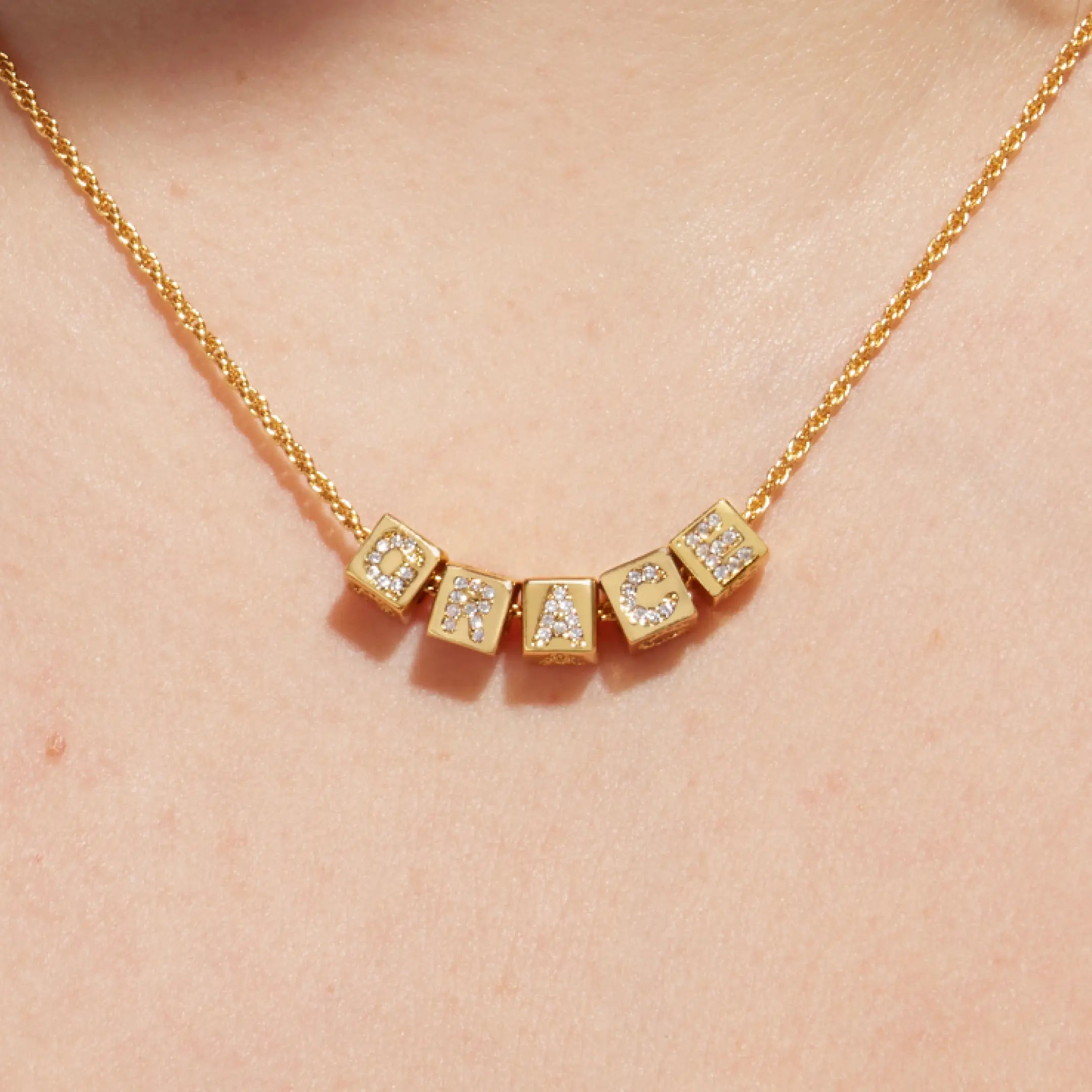 Gold necklace with CZ-encrusted letters on a person's neck