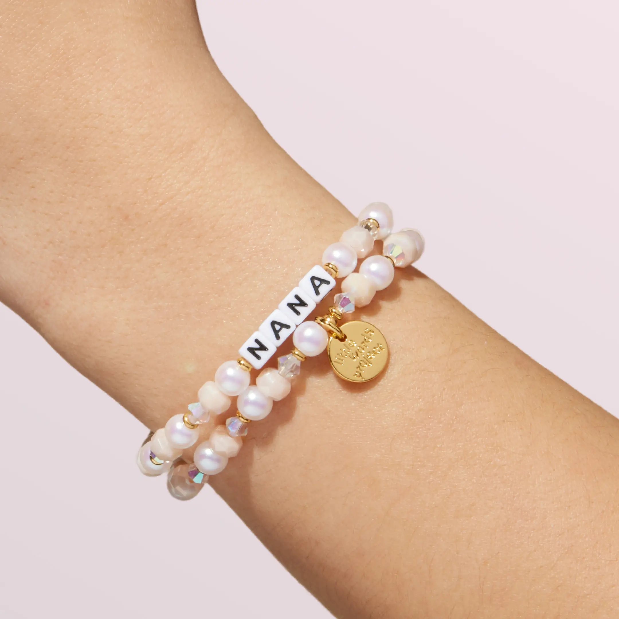 Pearl bracelet with 'Nana' on a wrist against a light pink background