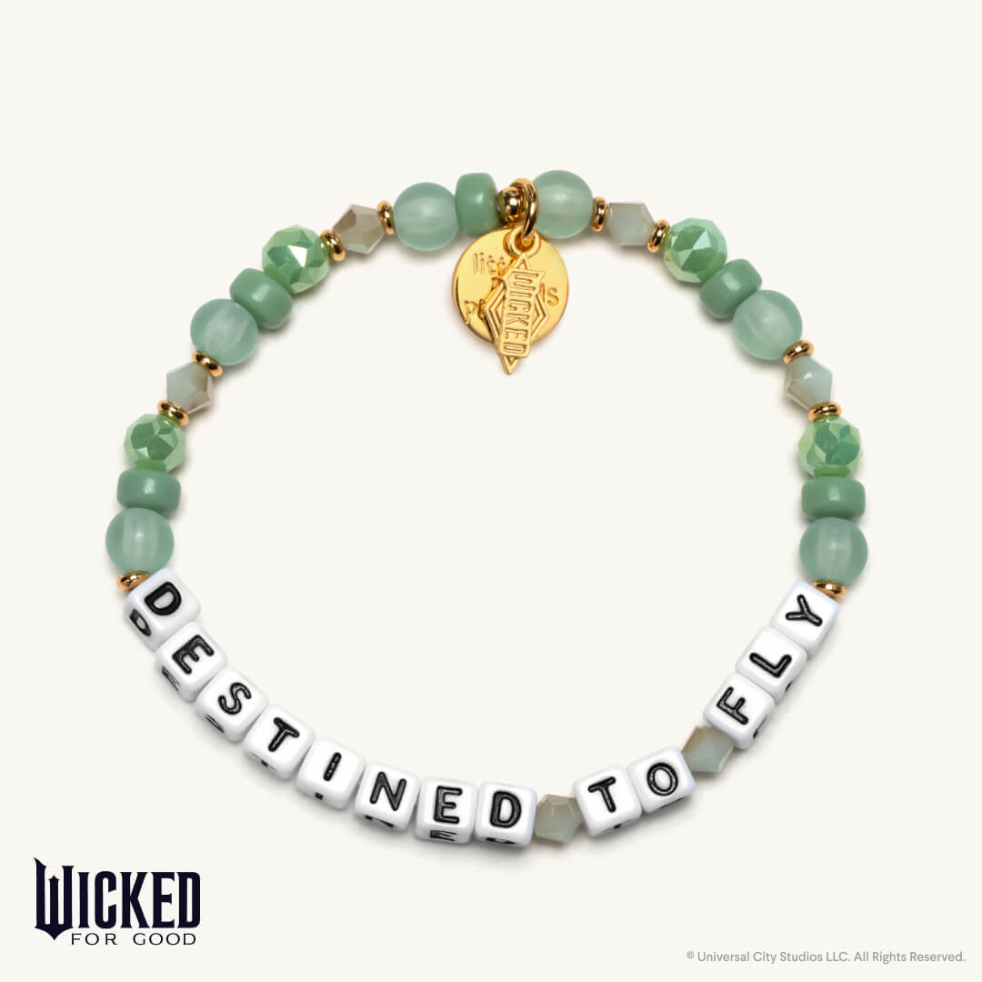 Bracelet with green beads and letter beads spelling 'Destined to Fly', featuring a gold tag, on a white background. Brand 'Wicked for Good' visible.