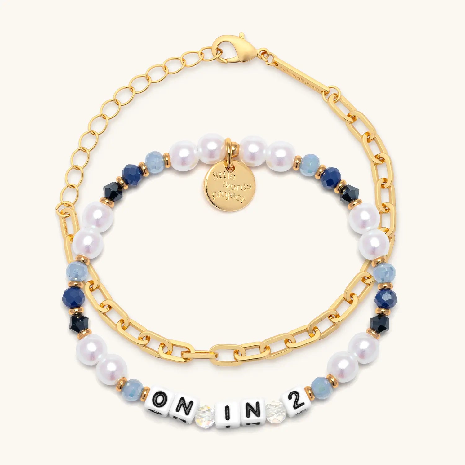 On In 2 bracelet set flat-lay — beaded bracelet with white pearls and navy crystals layered with gold chain link bracelet, cream background