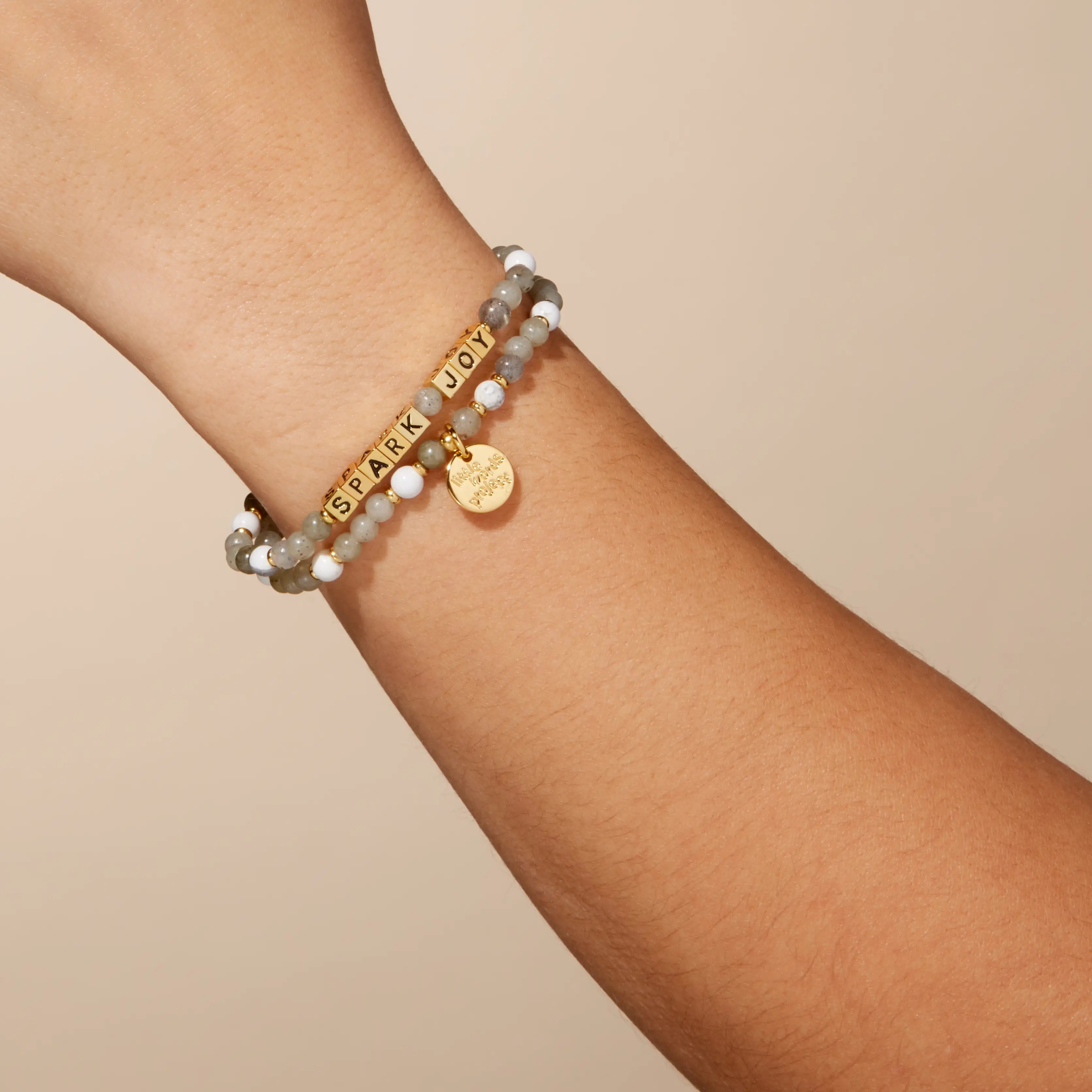 Bracelet with gold tag and text on wrist against a beige background