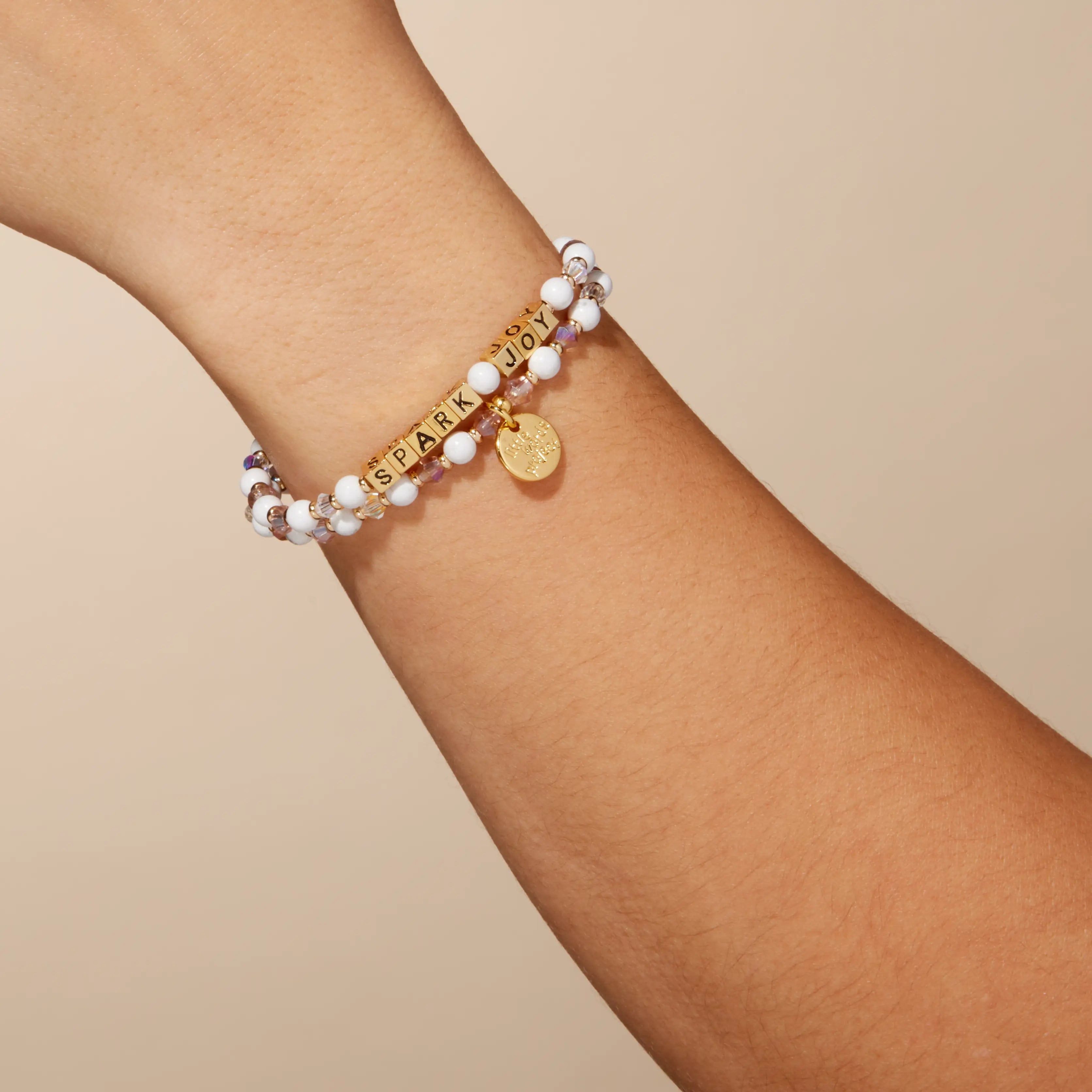 Bracelet with beads and a gold tag on a wrist against a beige background