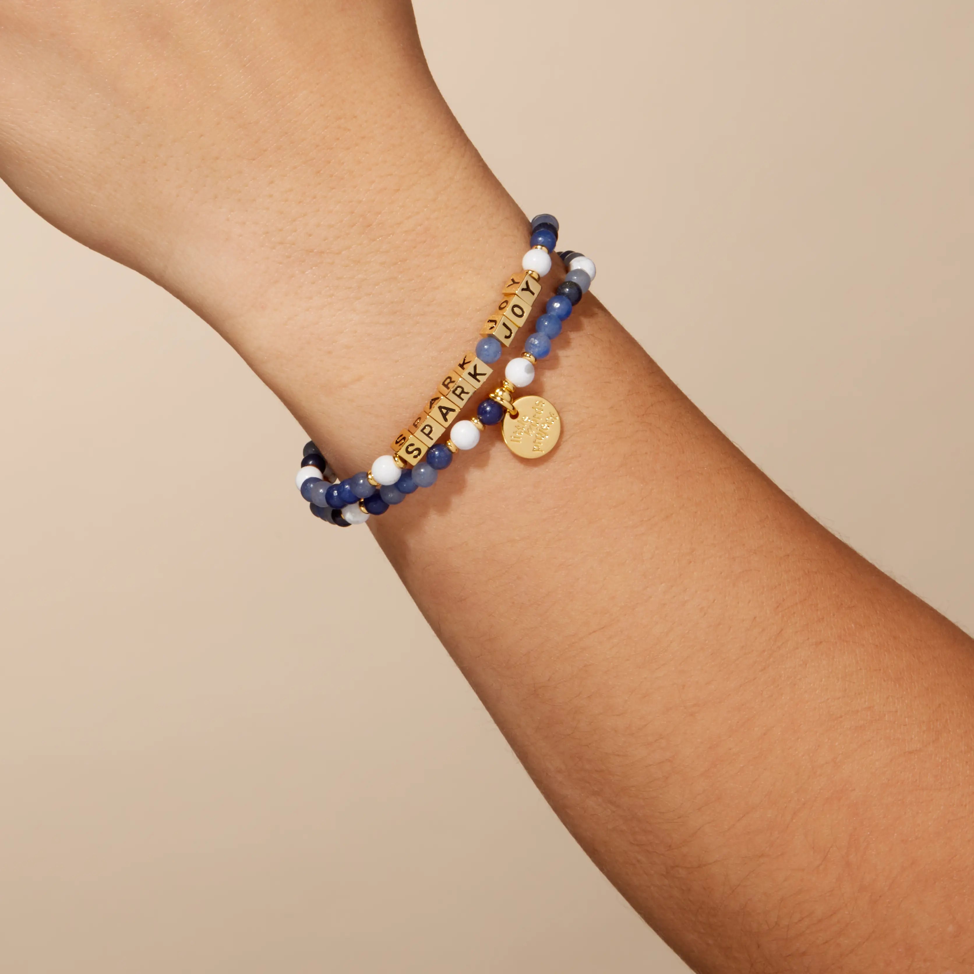 Bracelet with beads and gold charms on a wrist against a beige background
