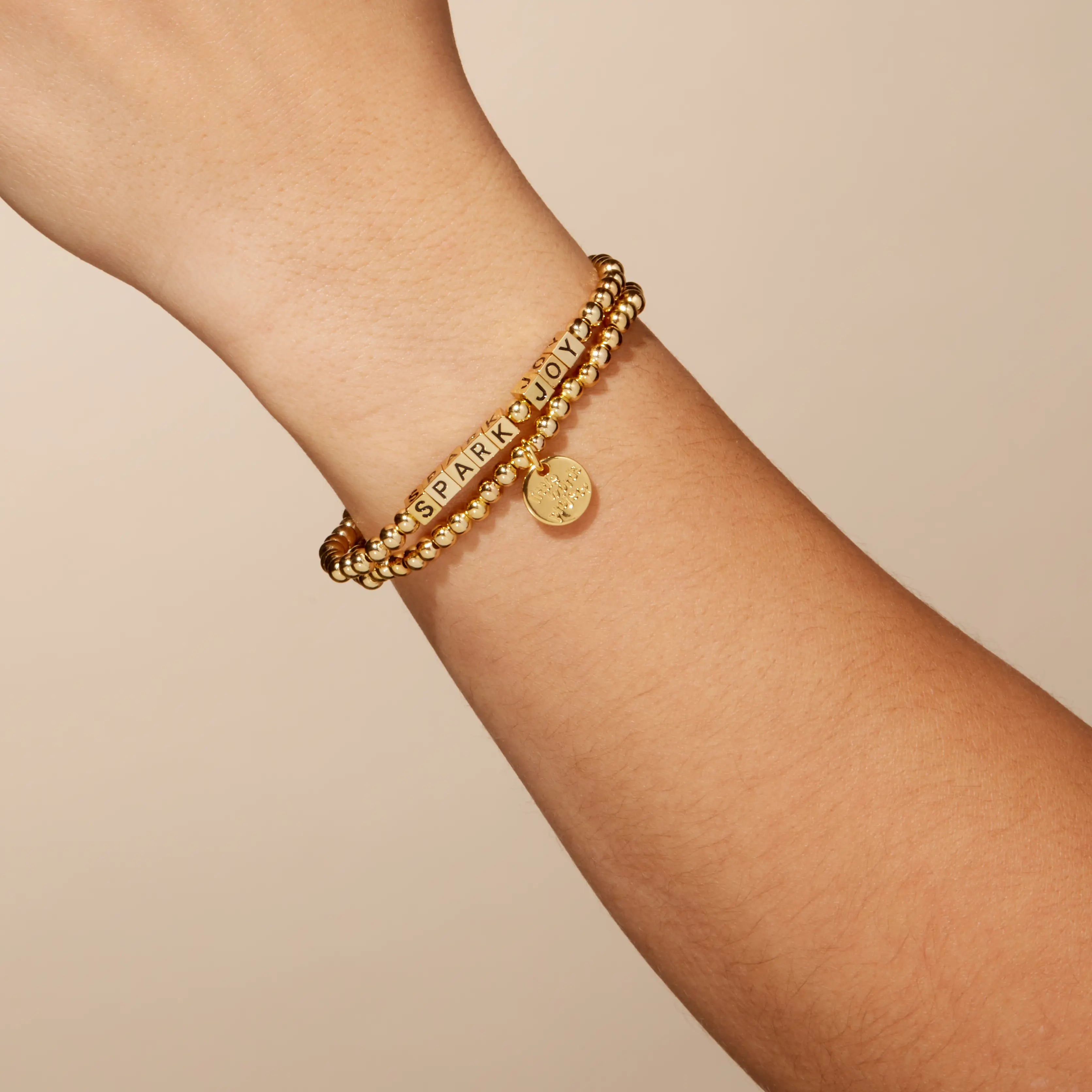 Gold bracelet on a wrist against a beige background