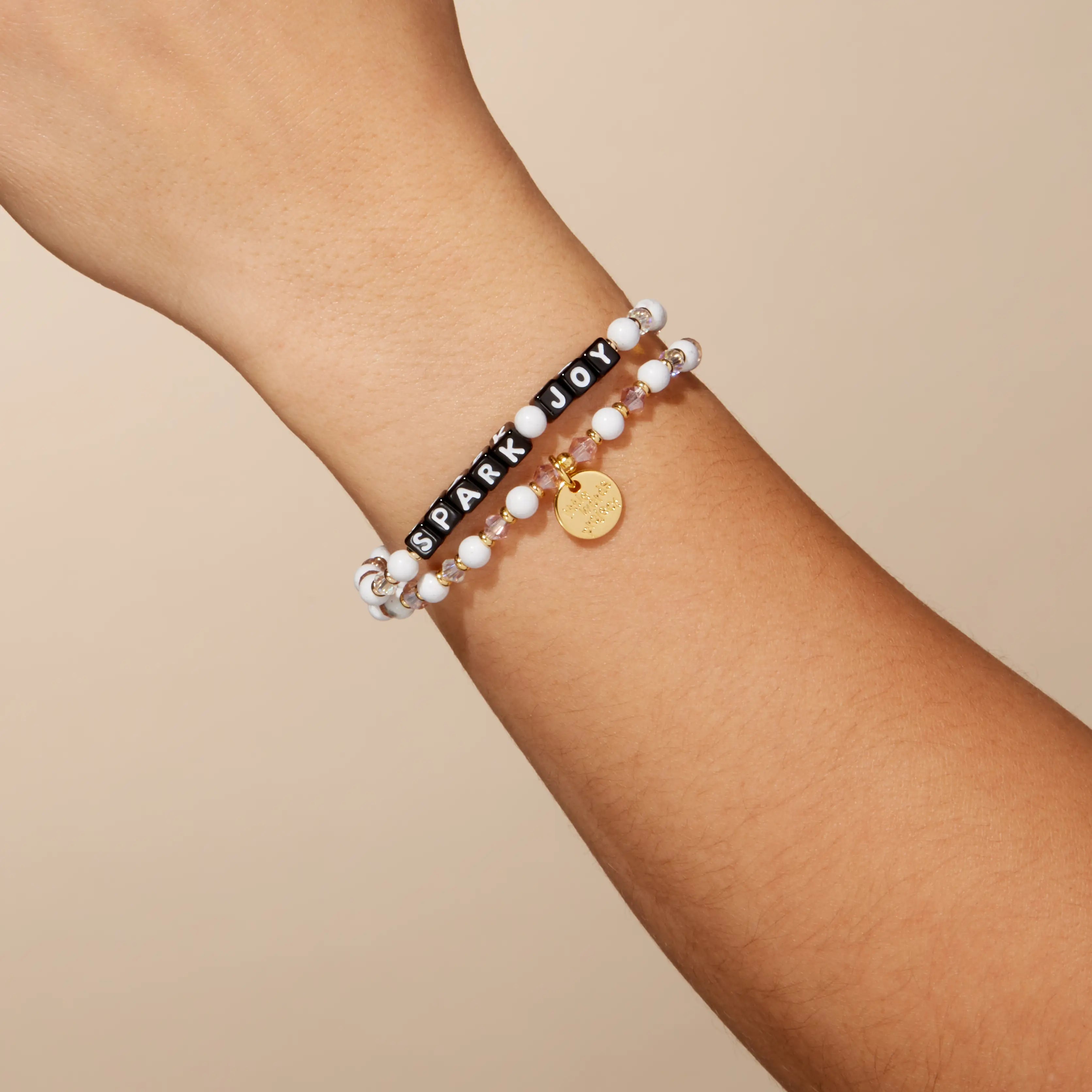 Bracelet with 'Spark Joy' charm on a wrist against a beige background