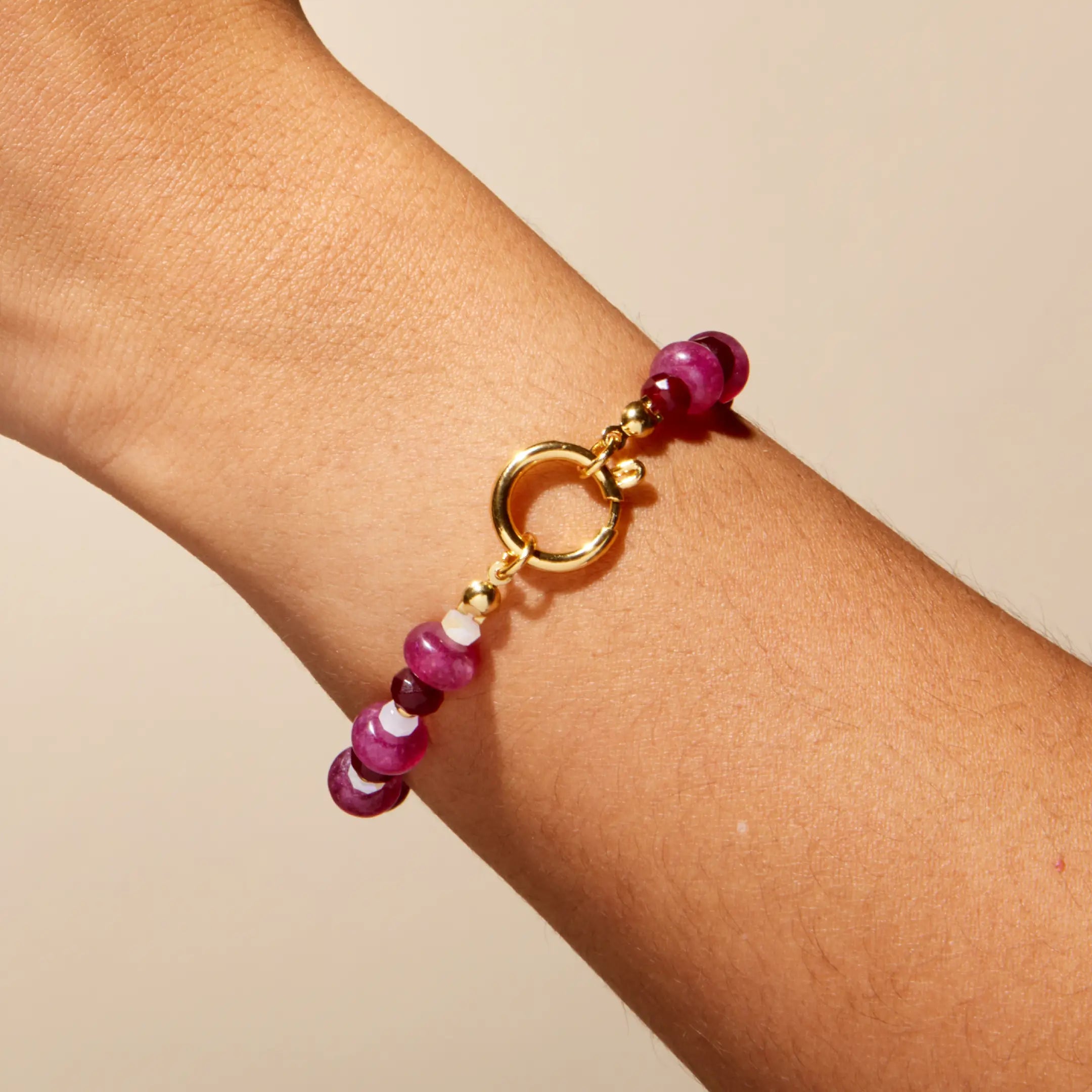 Beaded bracelet with pink and gold elements on a wrist against a beige background