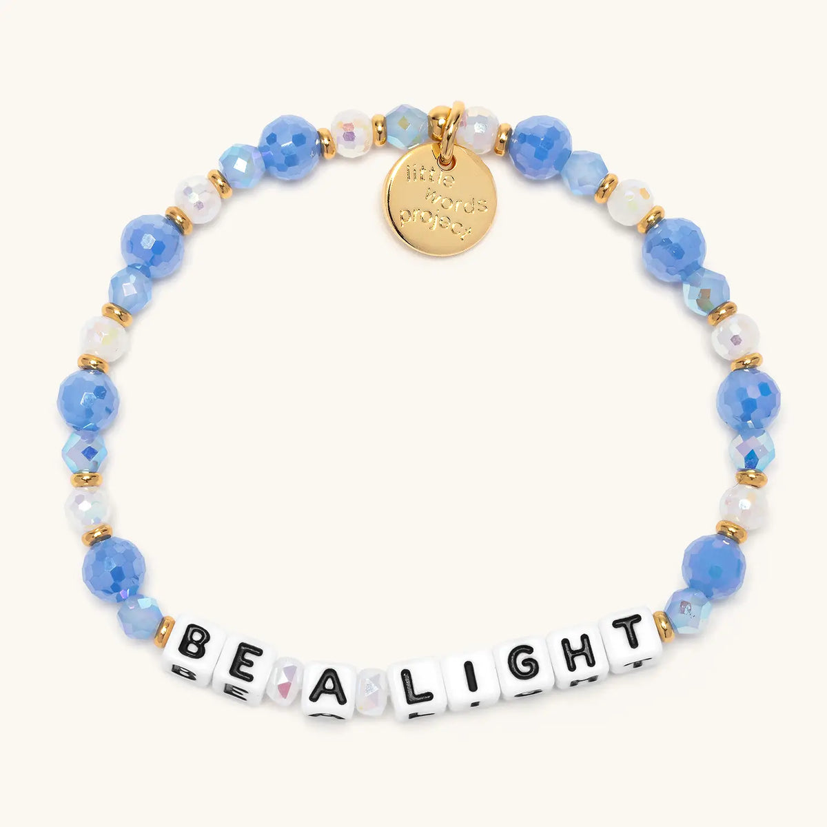 Be a Light bracelet in the Blizzard Baby bead pattern, white letter beads with periwinkle blue faceted beads, white beads, and clear iridescent crystals with gold accents, flat-lay on cream background