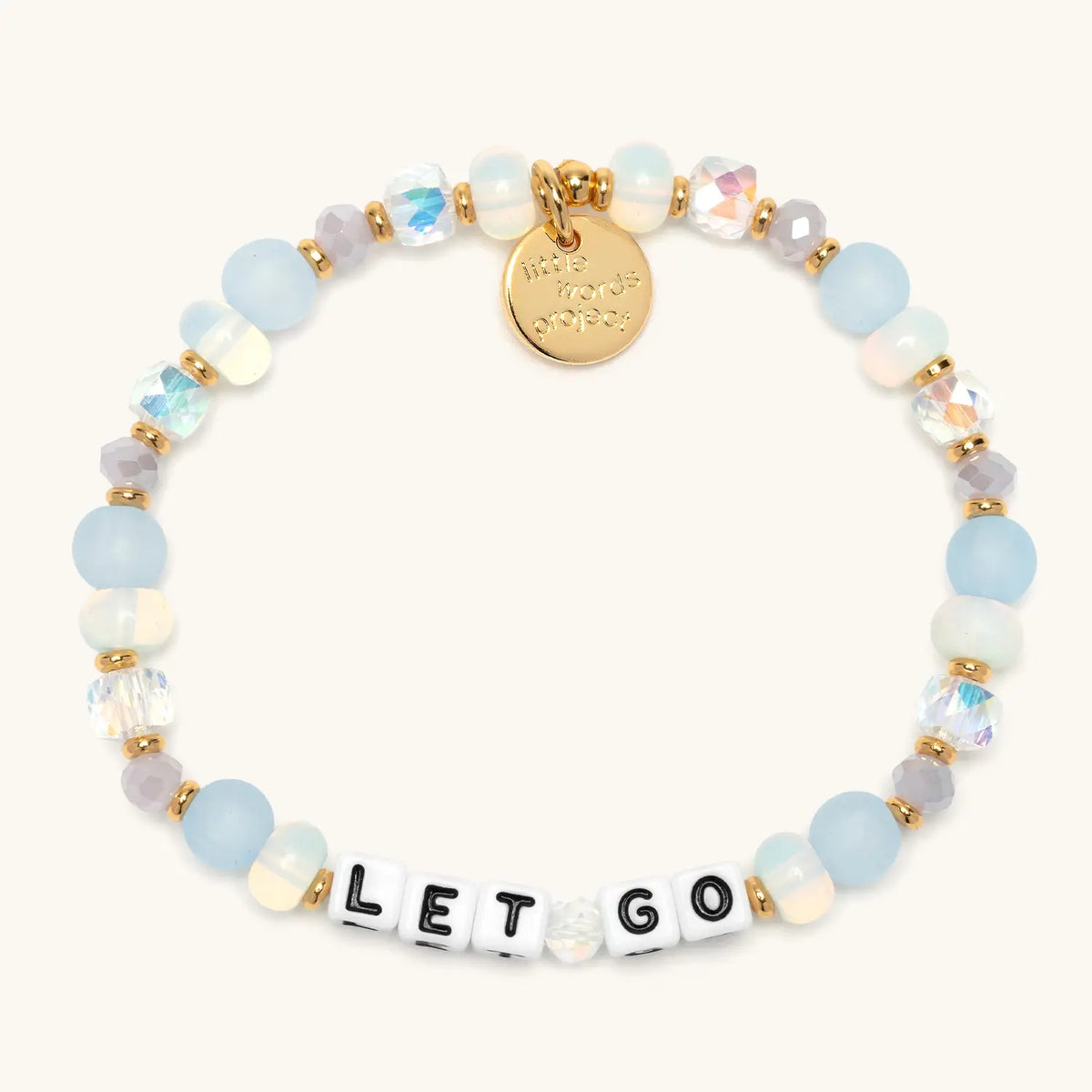 Let Go bracelet in the Marshmellow bead pattern, white letter beads with frosted light blue, opal, gray, and clear iridescent crystal beads with gold accents, flat-lay on cream background
