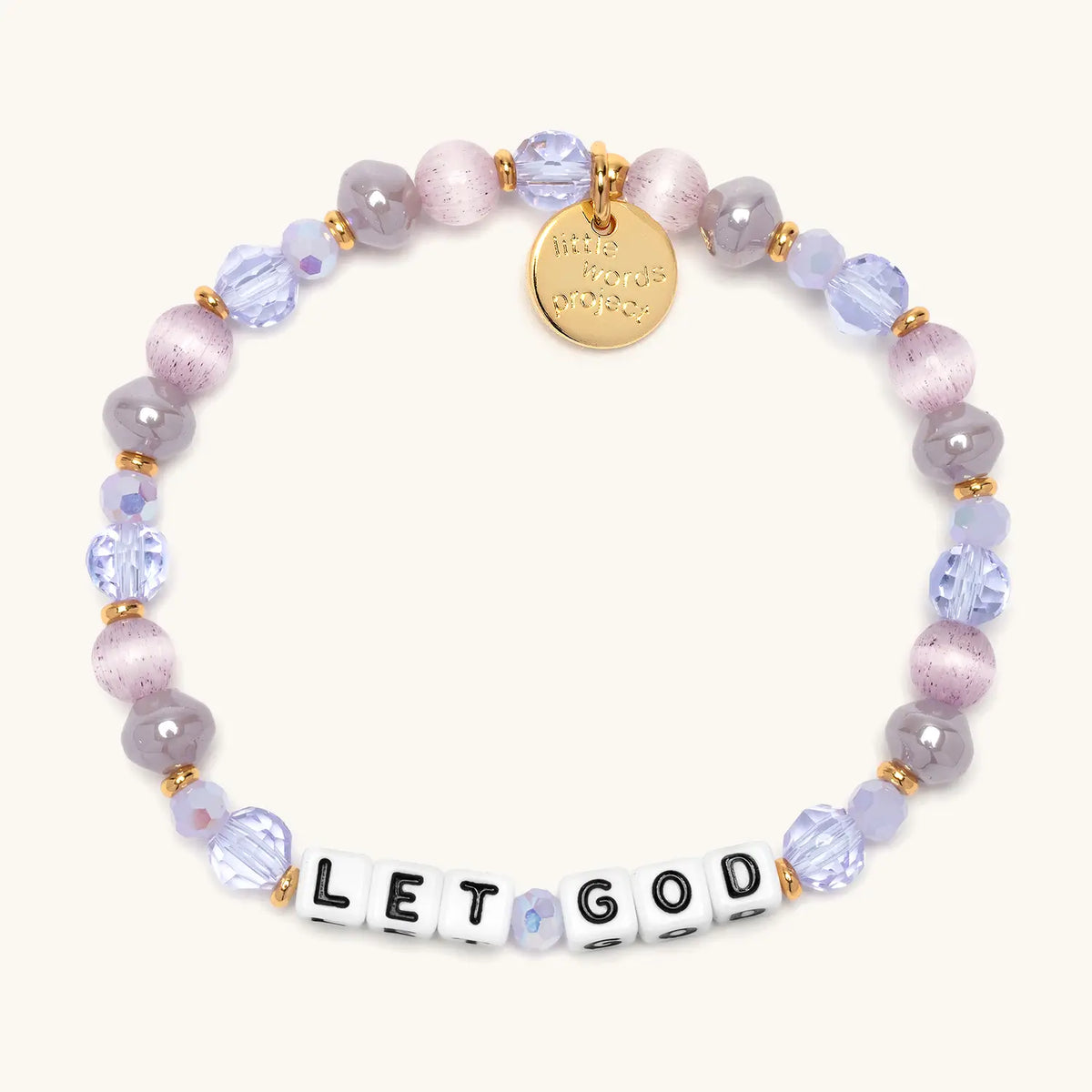 Let God bracelet in the Purple Twinkle bead pattern, white letter beads with lavender crystals, mauve cat's eye beads, and gray pearls with gold accents, flat-lay on cream background