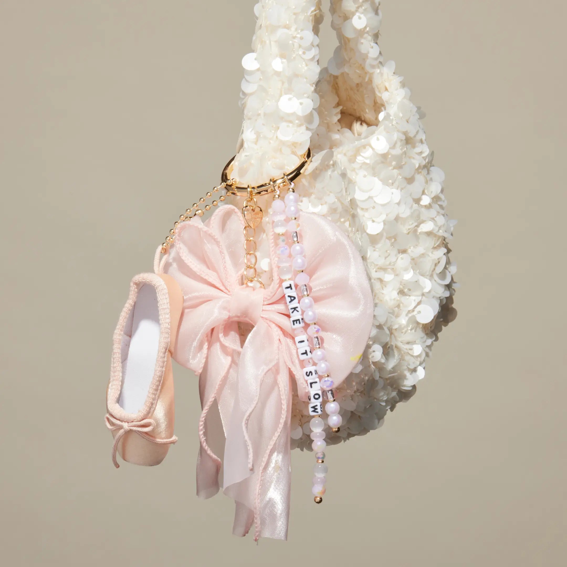 Take It Slow satin bow bag charm clipped to a white sequin bag