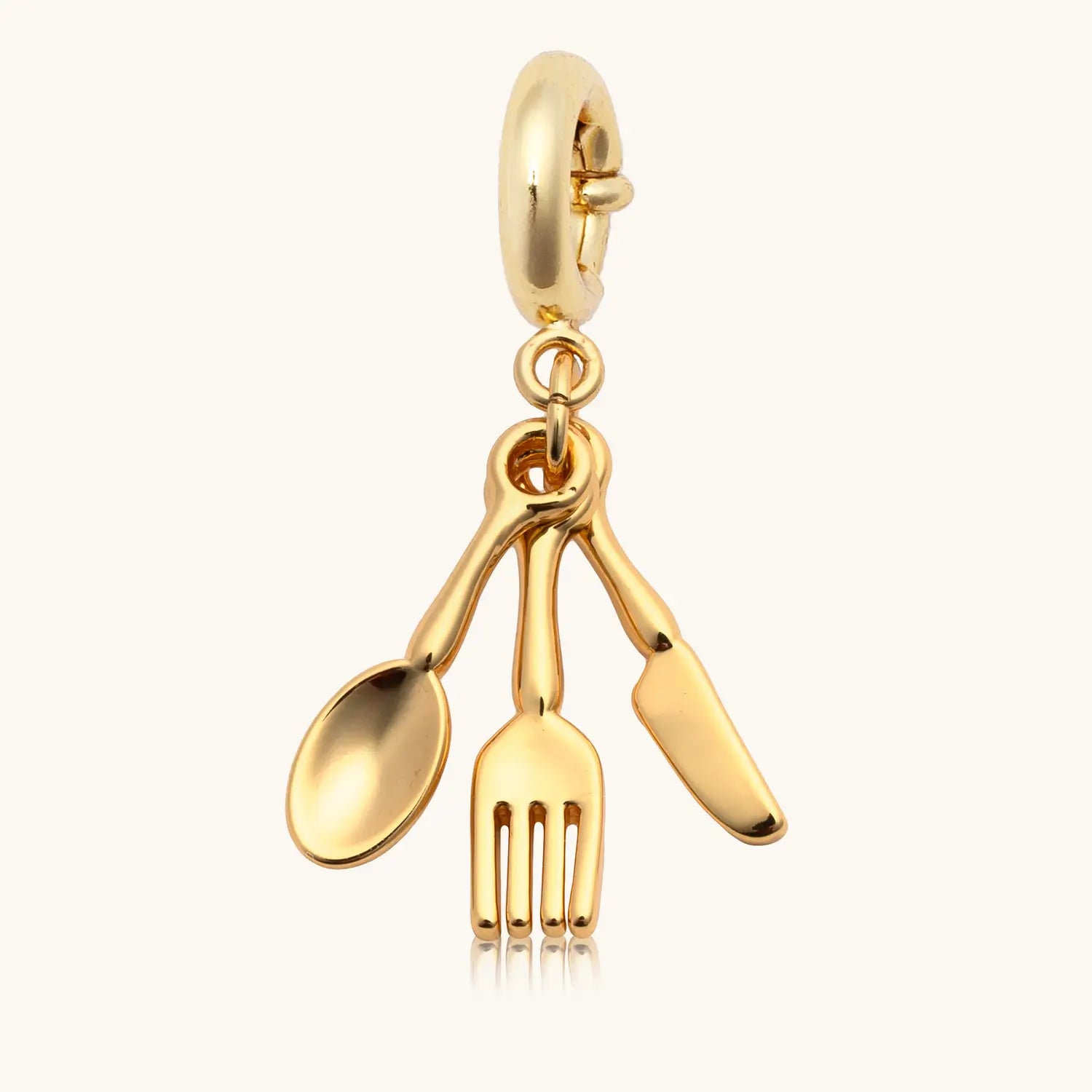 Gold charm shaped like a spoon, knife, and fork on a white background