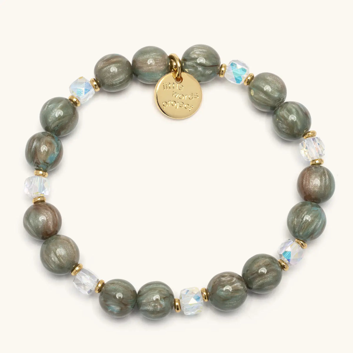 Velvet Voltage Bracelet Base in the Velvet Voltage bead pattern, marbled sage green beads with clear iridescent crystals, gold accents, and a gold logo coin tag, flat-lay on cream background