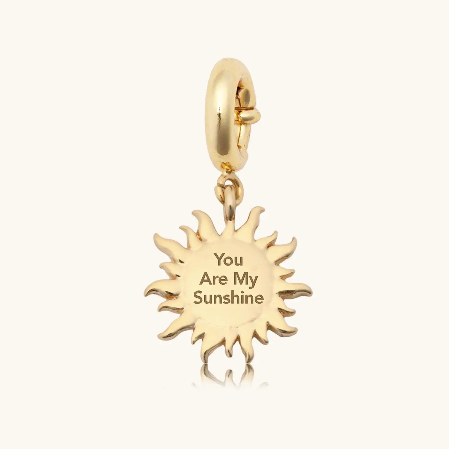 Reverse side of a gold sun-shaped charm pendant engraved with the text "You Are My Sunshine," featuring pointed ray details around the edge, hanging from a polished gold spring-ring clasp, on a light grey background.