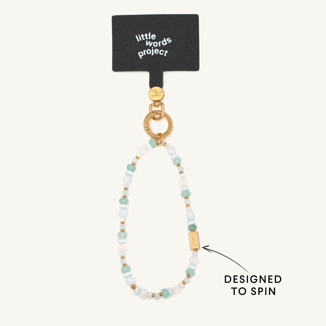 Little Words Project beaded phone strap in soft blue, white, and gold tones with a spinning gold bar charm.