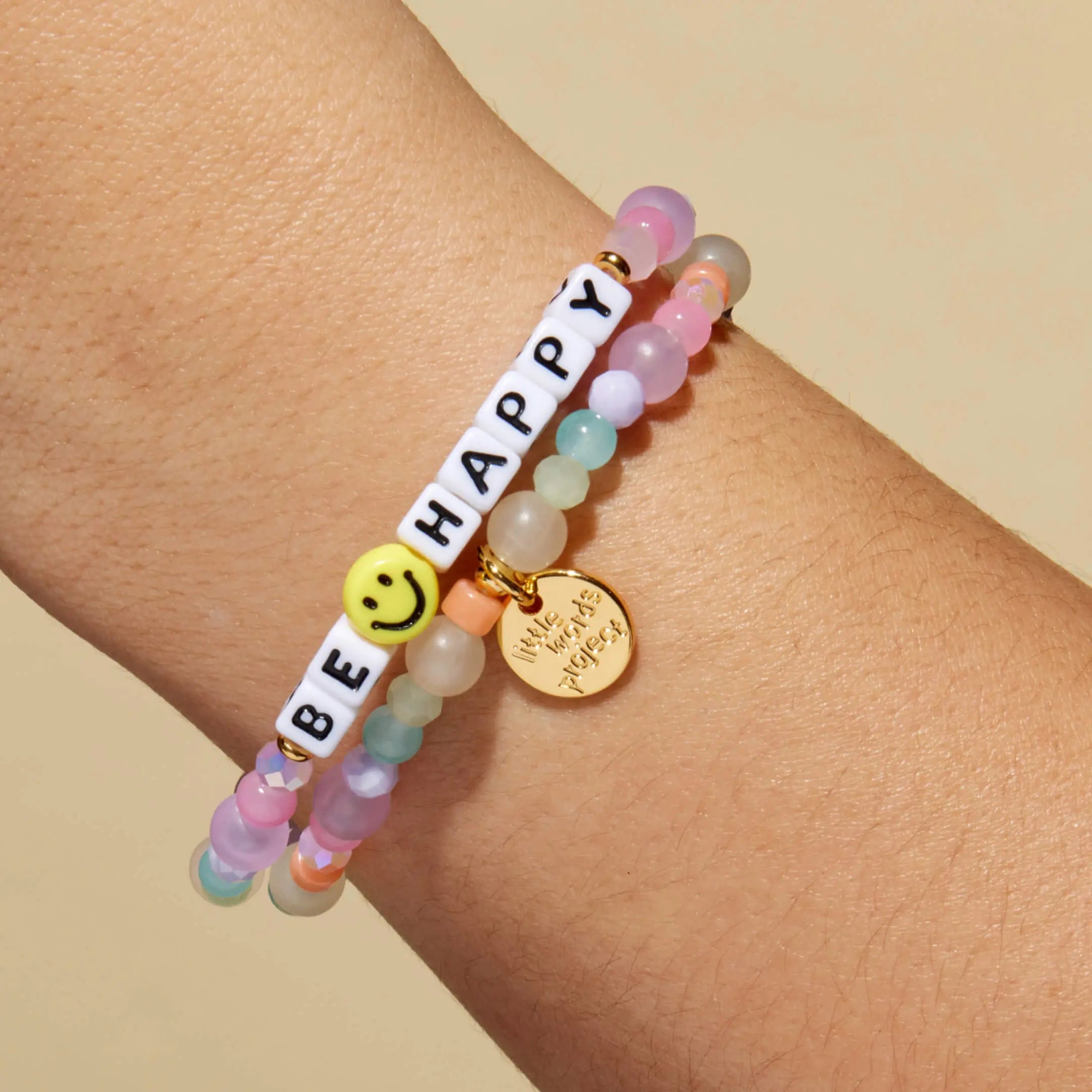 Colorful beaded bracelet with 'BE HAPPY' message on wrist against a beige background