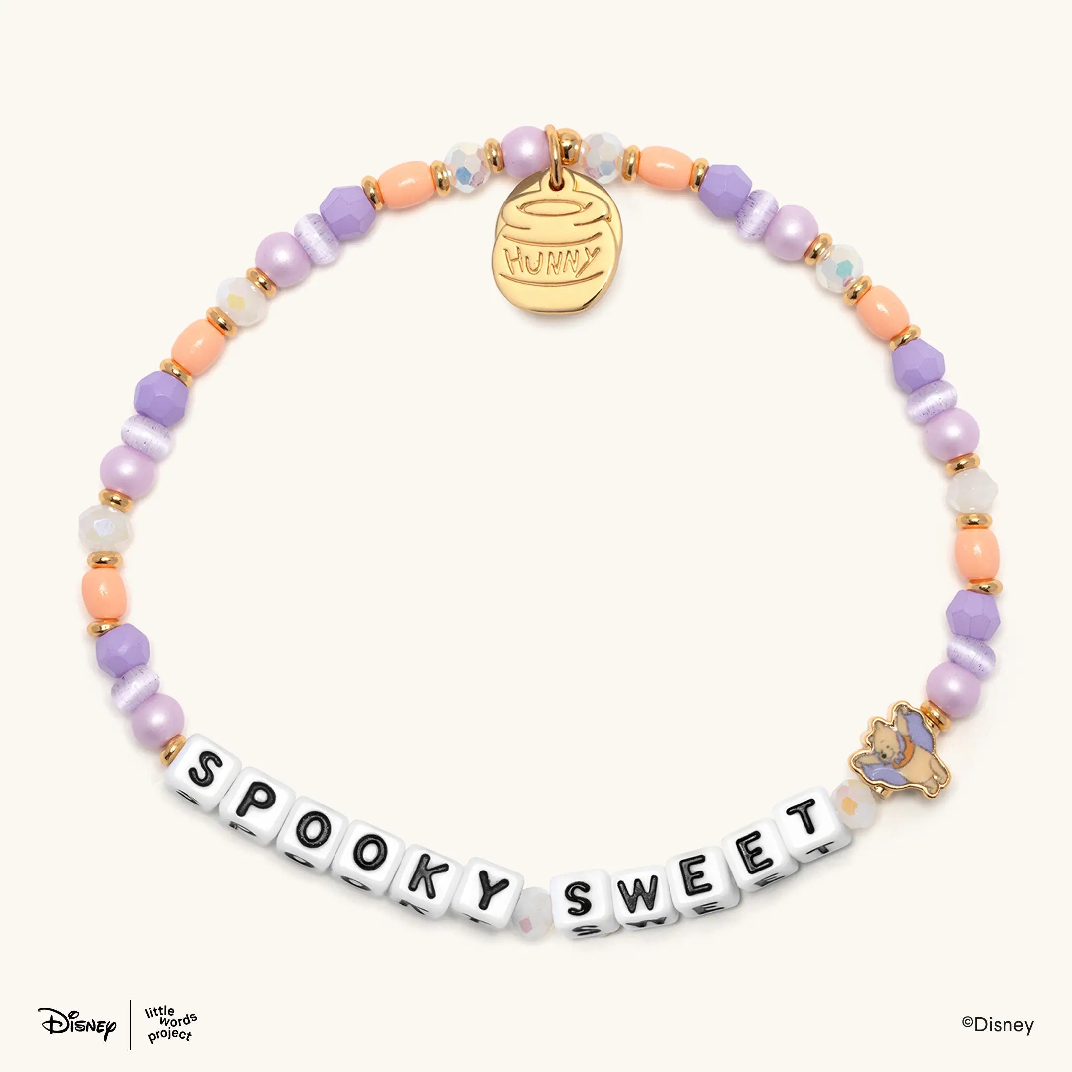 Spooky Sweet Disney's Winnie the Pooh beaded bracelet in lavender, soft orange, and cat eye glass beads with white letter beads and a gold Winnie the Pooh vampire casted bead, flat-lay