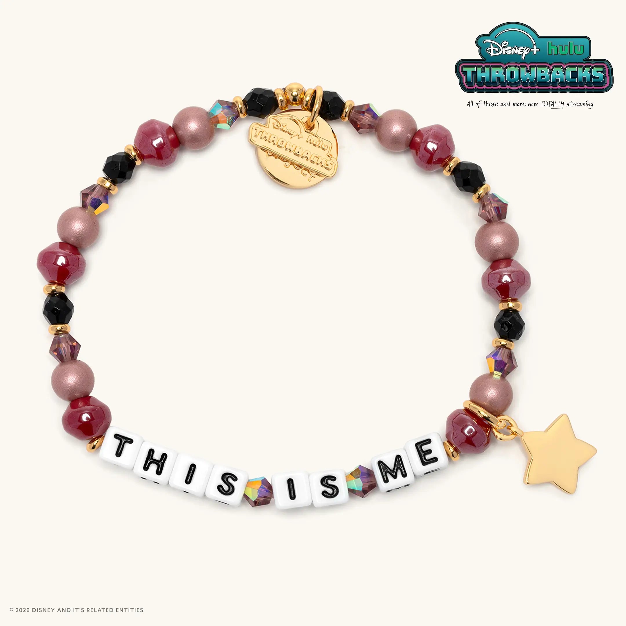 This Is Me Disney+ Hulu Throwbacks bracelet with burgundy, black, and dusty mauve pearl beads, white letter beads, and a gold star charm, flat lay on cream