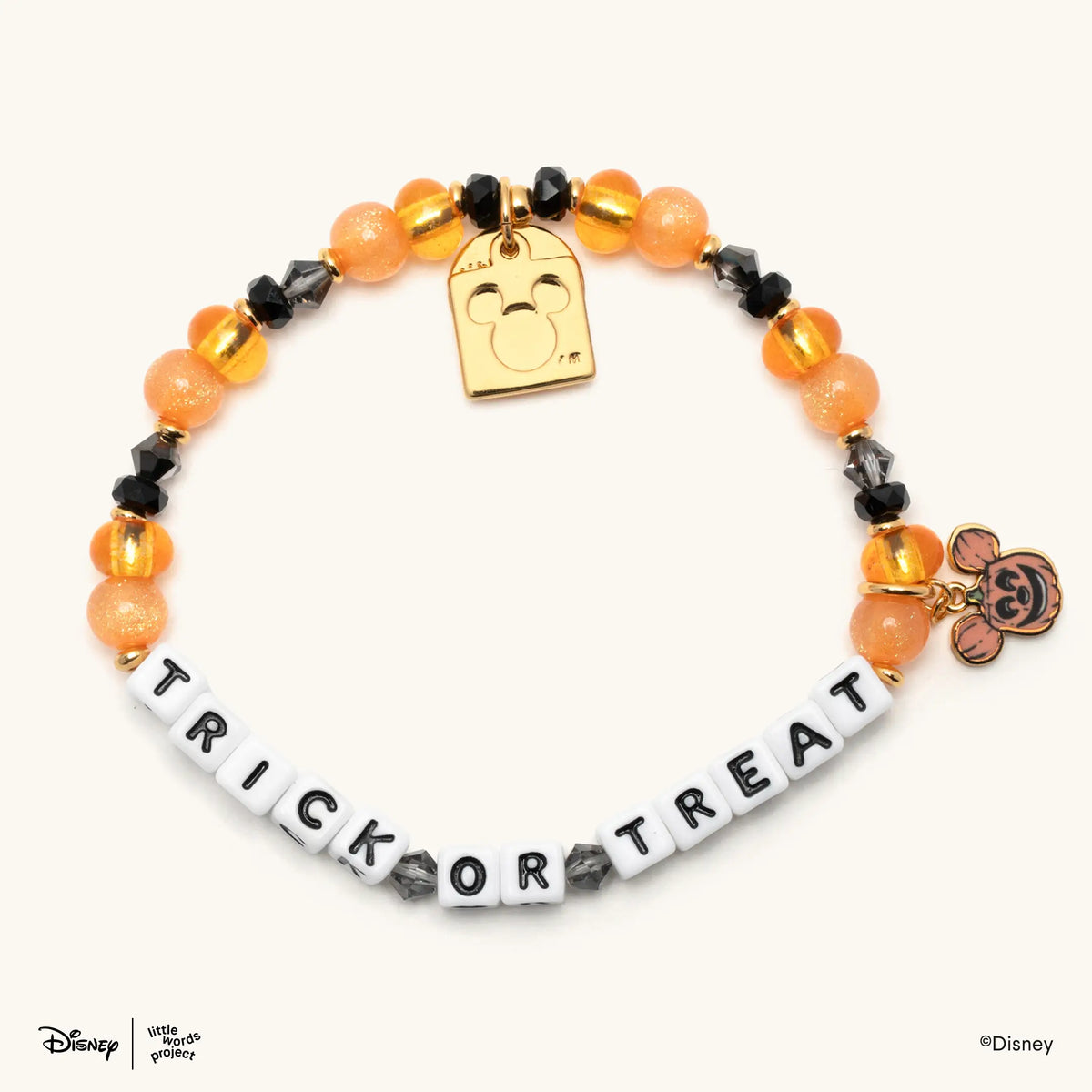 Trick or Treat Disney's Mickey & Friends beaded bracelet in orange and black beads with white letter beads and a gold Mickey Mouse pumpkin charm, flat-lay