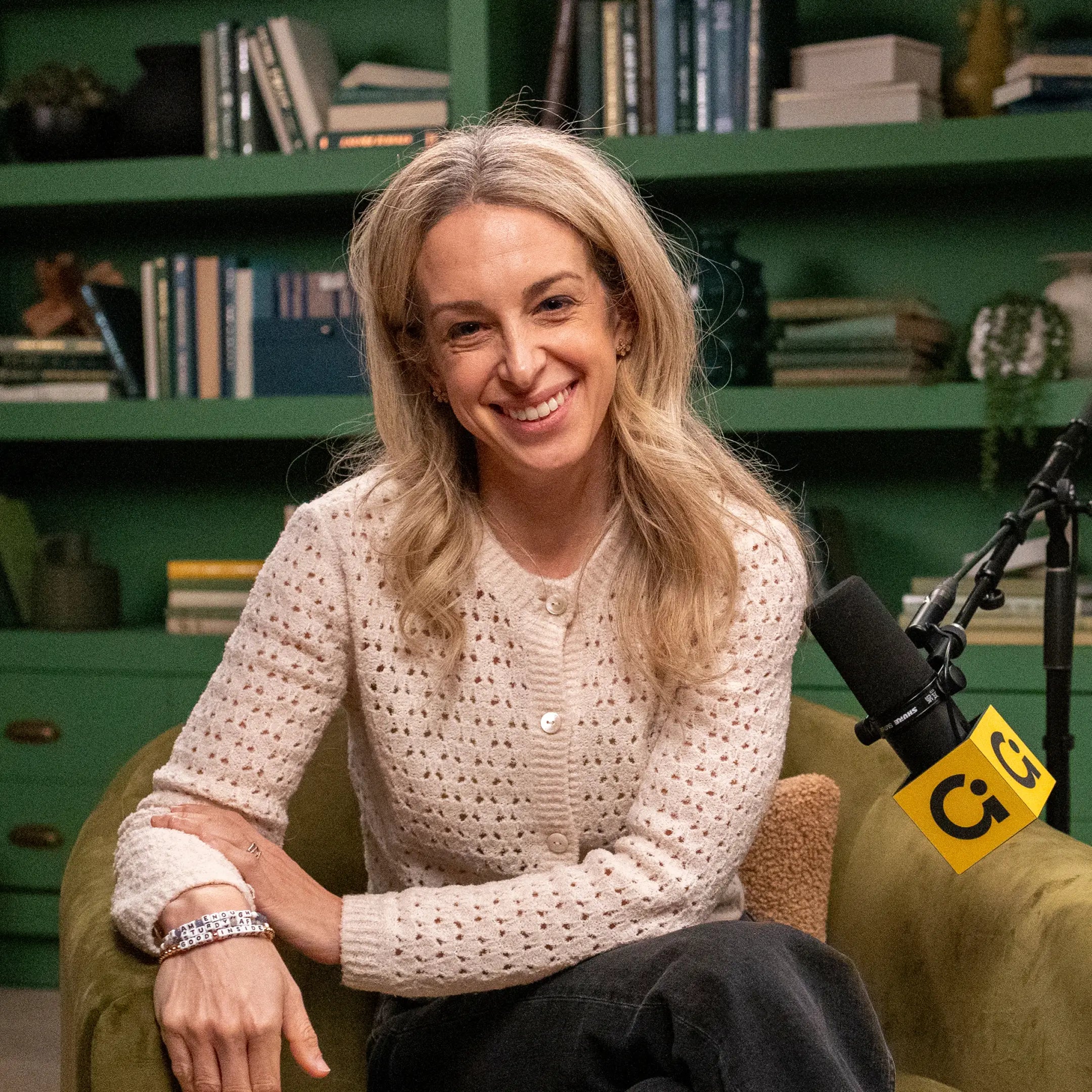 Woman sitting in a chair with a microphone in a room with bookshelves.