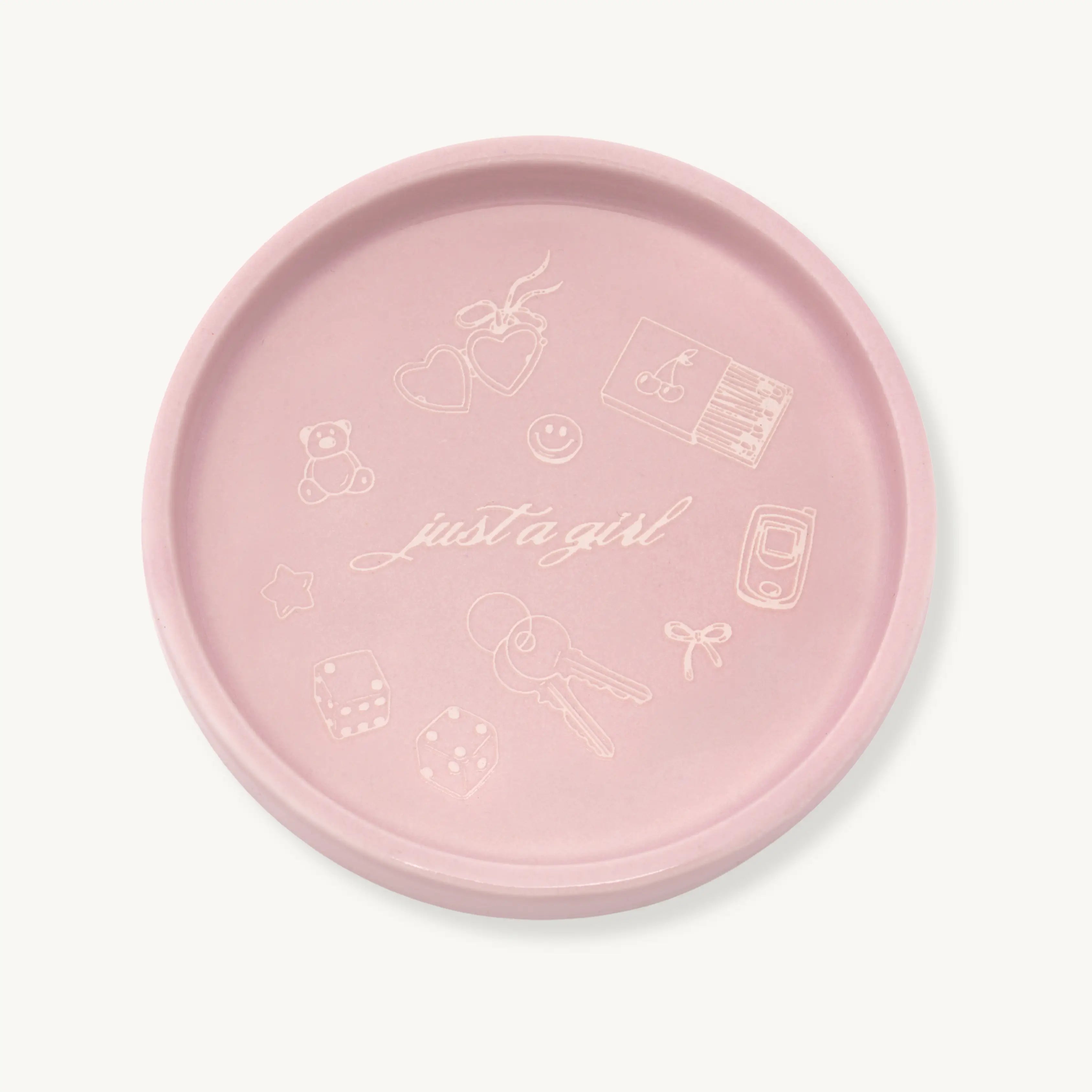 Pink jewelry dish with decorative icons and 'just a girl' text on a light tan background
