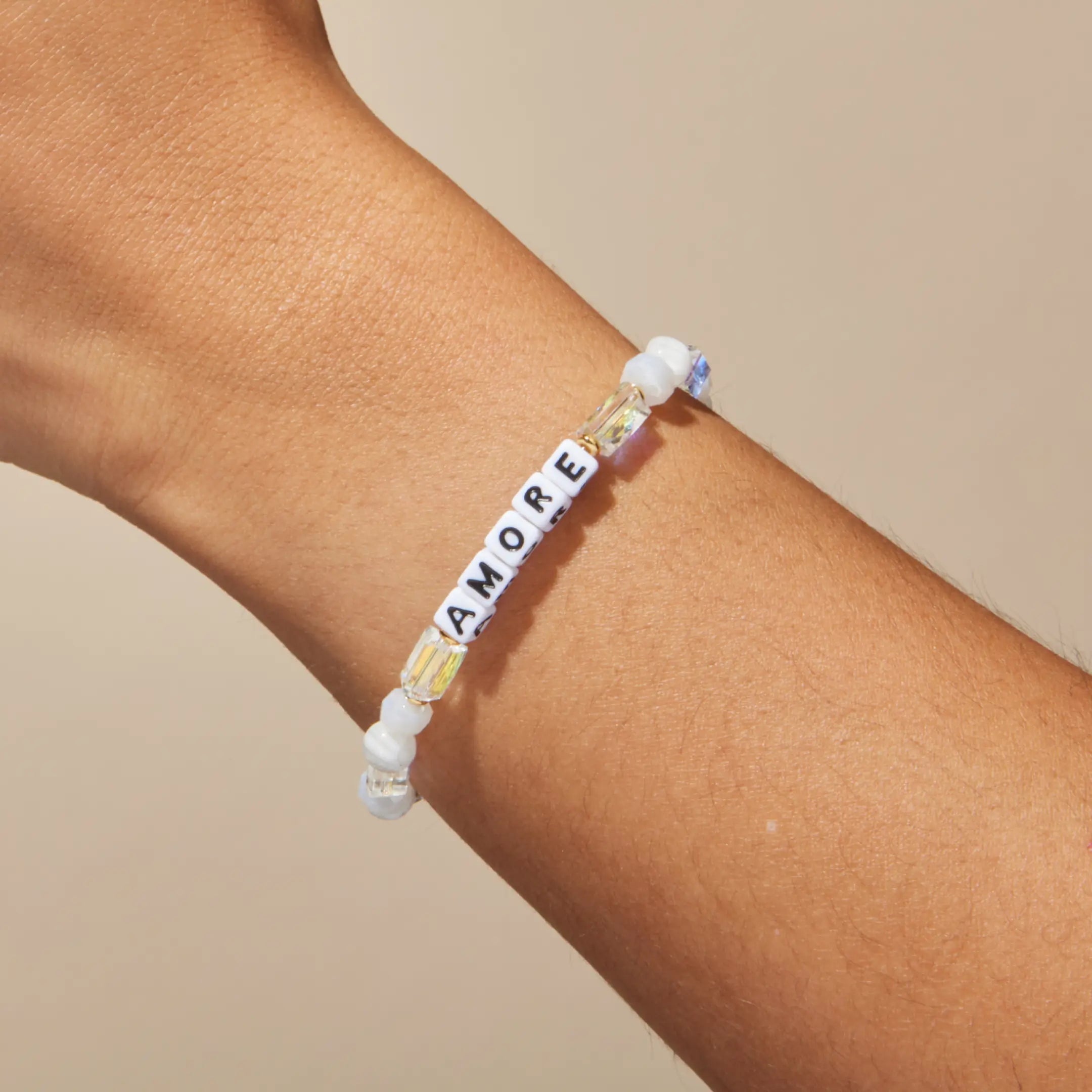 Bracelet with 'AMORE' beads on a wrist against a beige background
