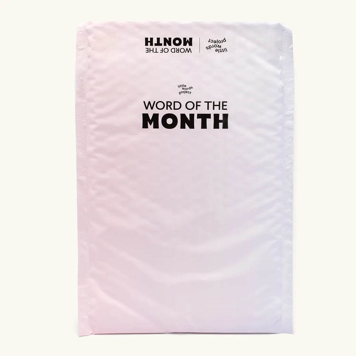 Back of the pink and white Little Words Project Word of the Month bubble mailer with black Word of the Month logo, packaging on cream background