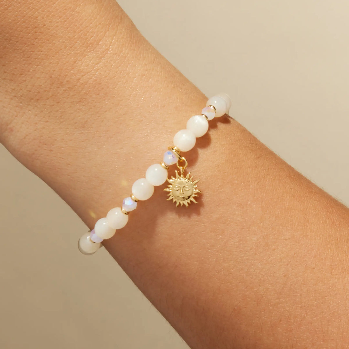 Sunshine Bracelet Base by Anna Sitar on wrist, white resin cat eye and iridescent crystal beads with a gold sun charm, on-model