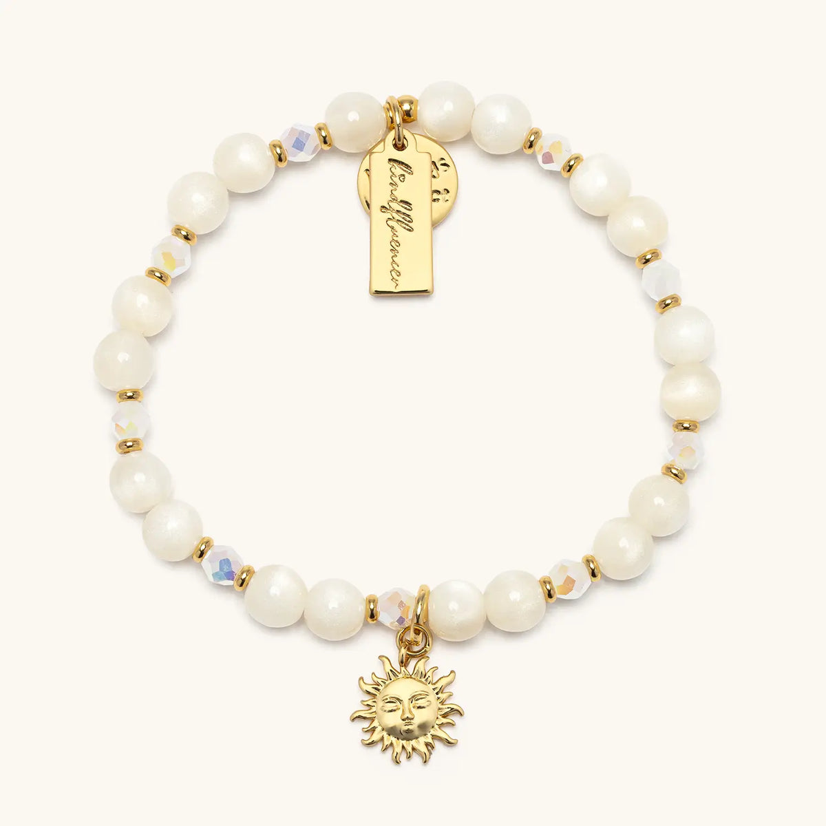 Sunshine Bracelet Base by Anna Sitar in the Enchanted Rose bead pattern, white resin cat eye and iridescent crystal beads with a gold sun charm and gold Kindfluencer tag, flat-lay on cream background