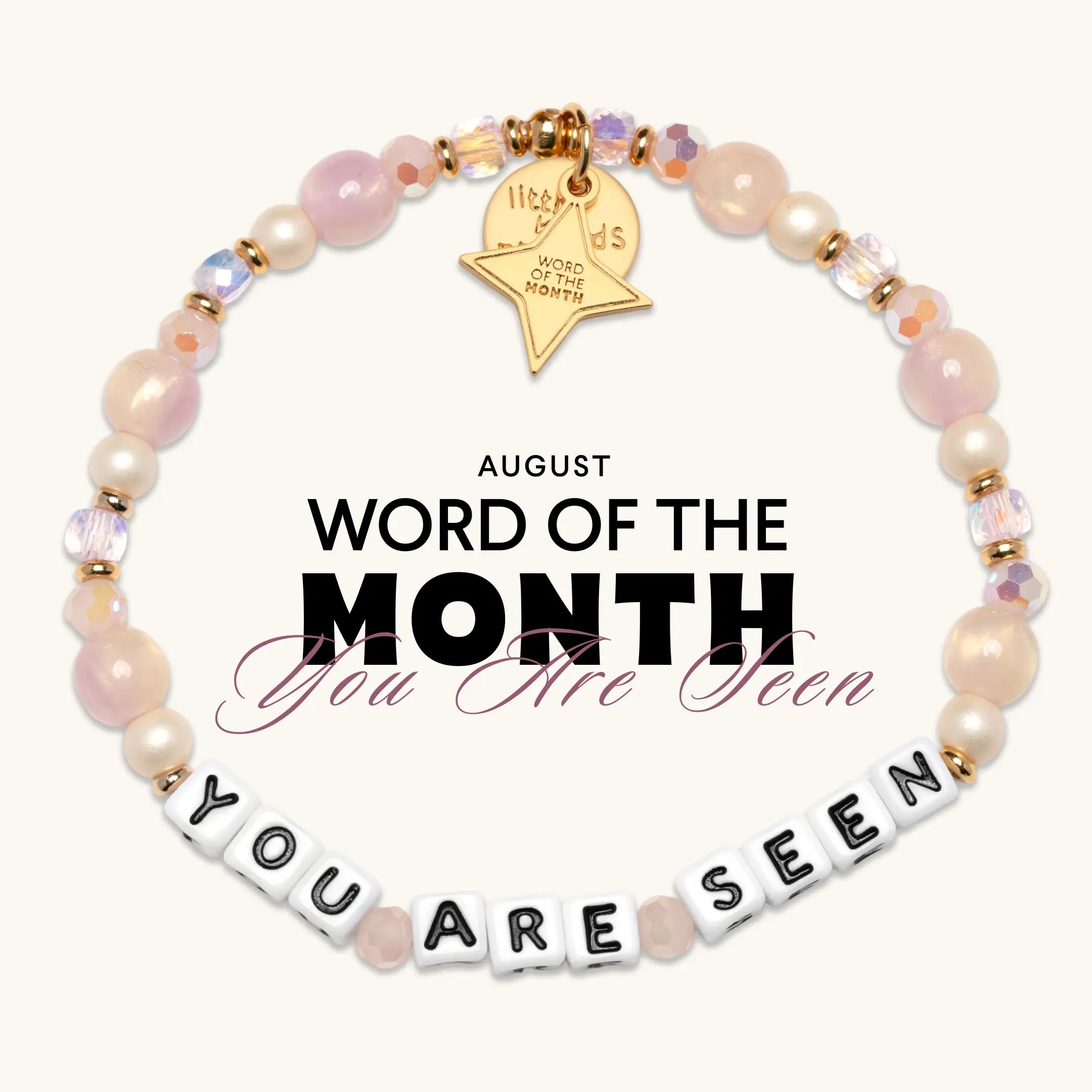 You Are Seen August Word of the Month bracelet with pink and cream beads, white letter beads, and a gold Word of the Month star charm