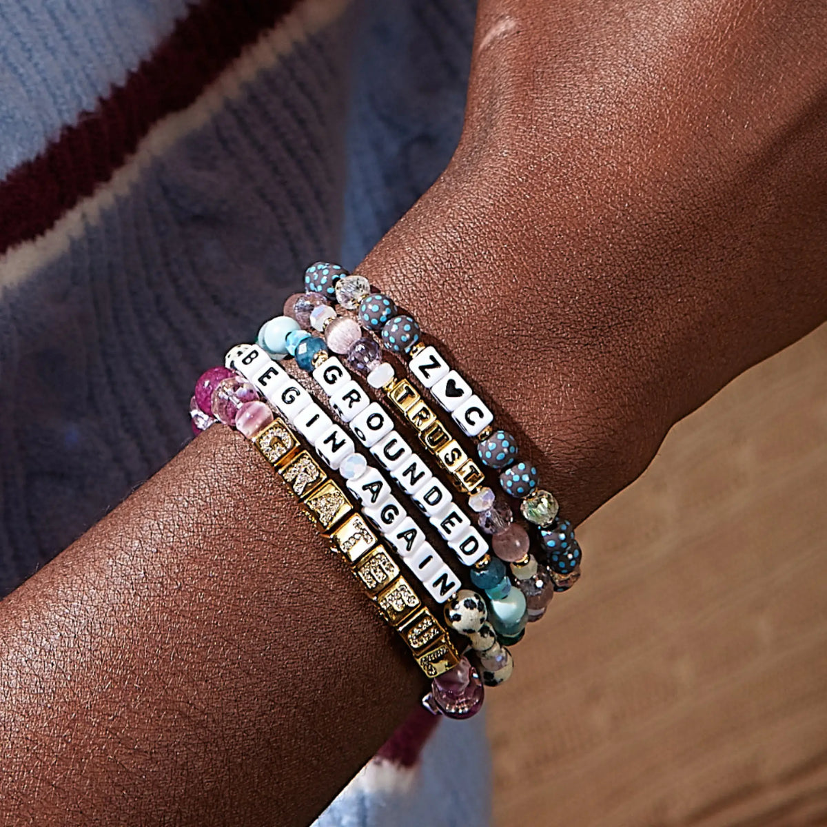 Stack of custom word bracelets worn on a wrist spelling Begin Again, Grateful, Grounded, Trust, and Z heart C, in dalmatian jasper and polka dot bead patterns