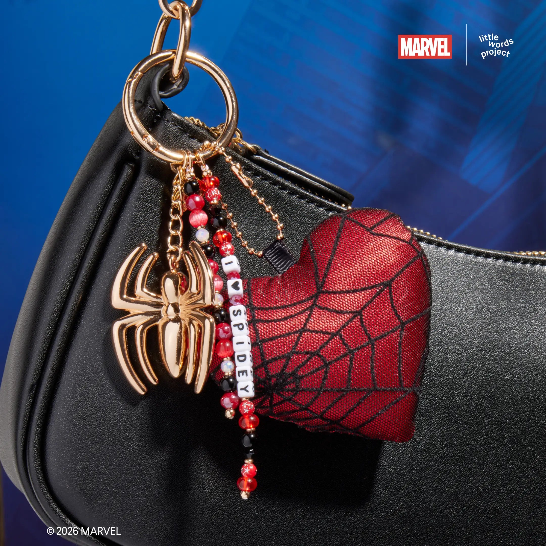 I Heart Spidey Bag Charm from Marvel's Spider-Man collection attached to black shoulder bag, on-model close-up showing gold spider charm with red spider-web heart plush and beaded I Heart Spidey strand