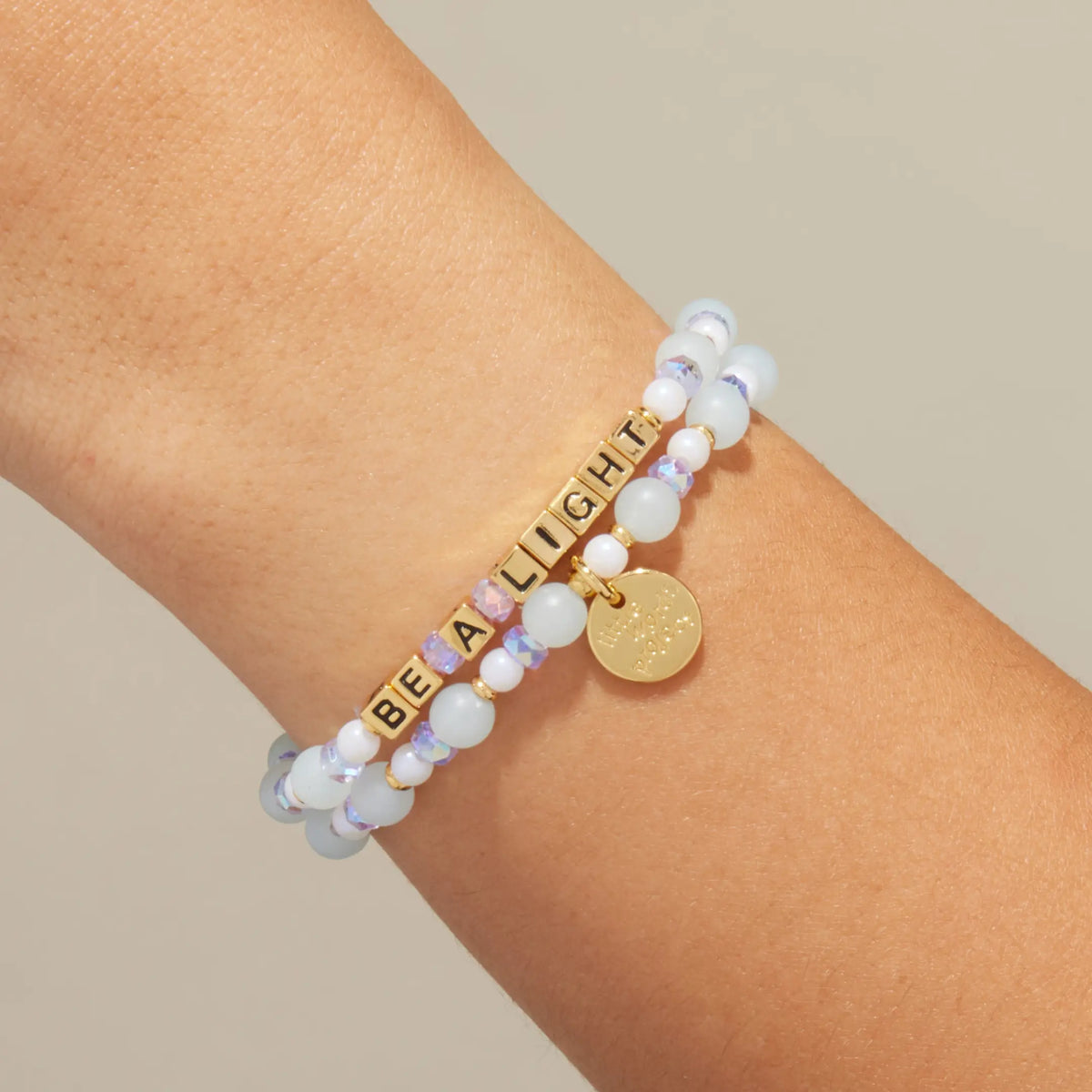 Gold Be a Light bracelet in the Honeydew Kiss bead pattern with gold letter beads, stacked with a coordinating beaded bracelet, on-model on wrist against cream background