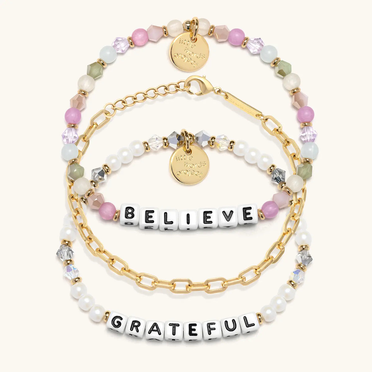 Little Reminders Bracelet Set in white letter beads, flat-lay on cream background showing Believe in orchid, mint and blush beads, the 14k gold-plated Paperclip Bracelet Base, and Grateful in white faux pearls and smoky crystals