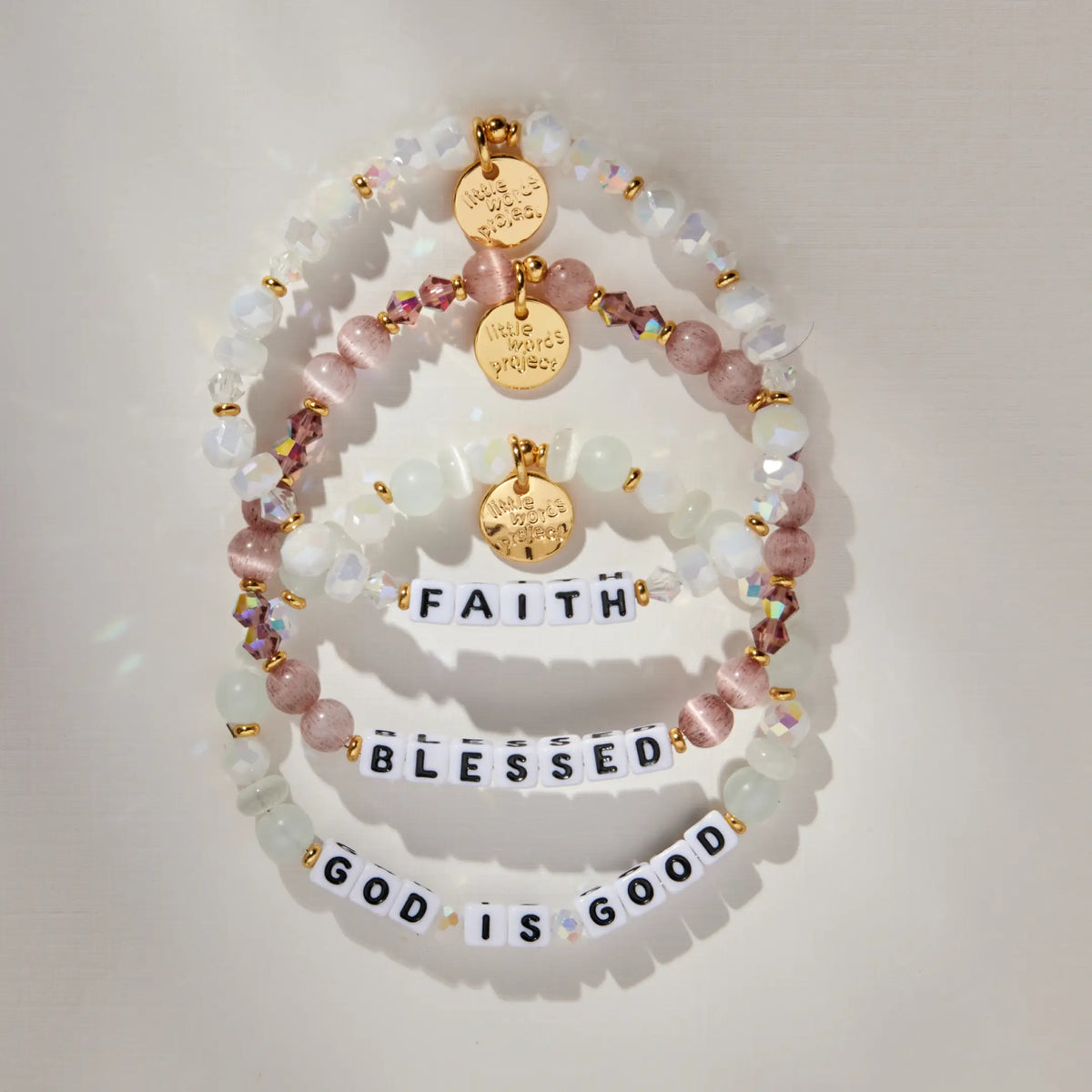 Faith Bracelet Set with the Faith, Blessed, and God is Good bracelets stacked, lifestyle flat-lay on warm neutral background with soft light